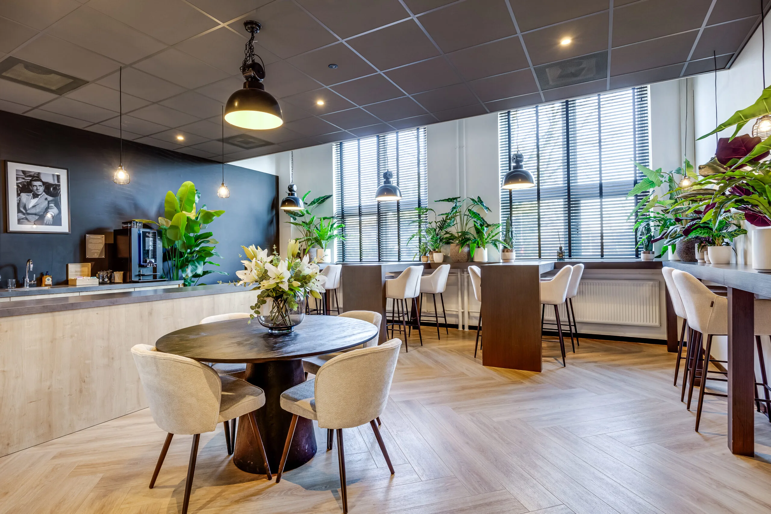 Modern lounge area on Lage Naarderweg with wooden flooring, cozy seating, indoor plants, and large windows with blinds.