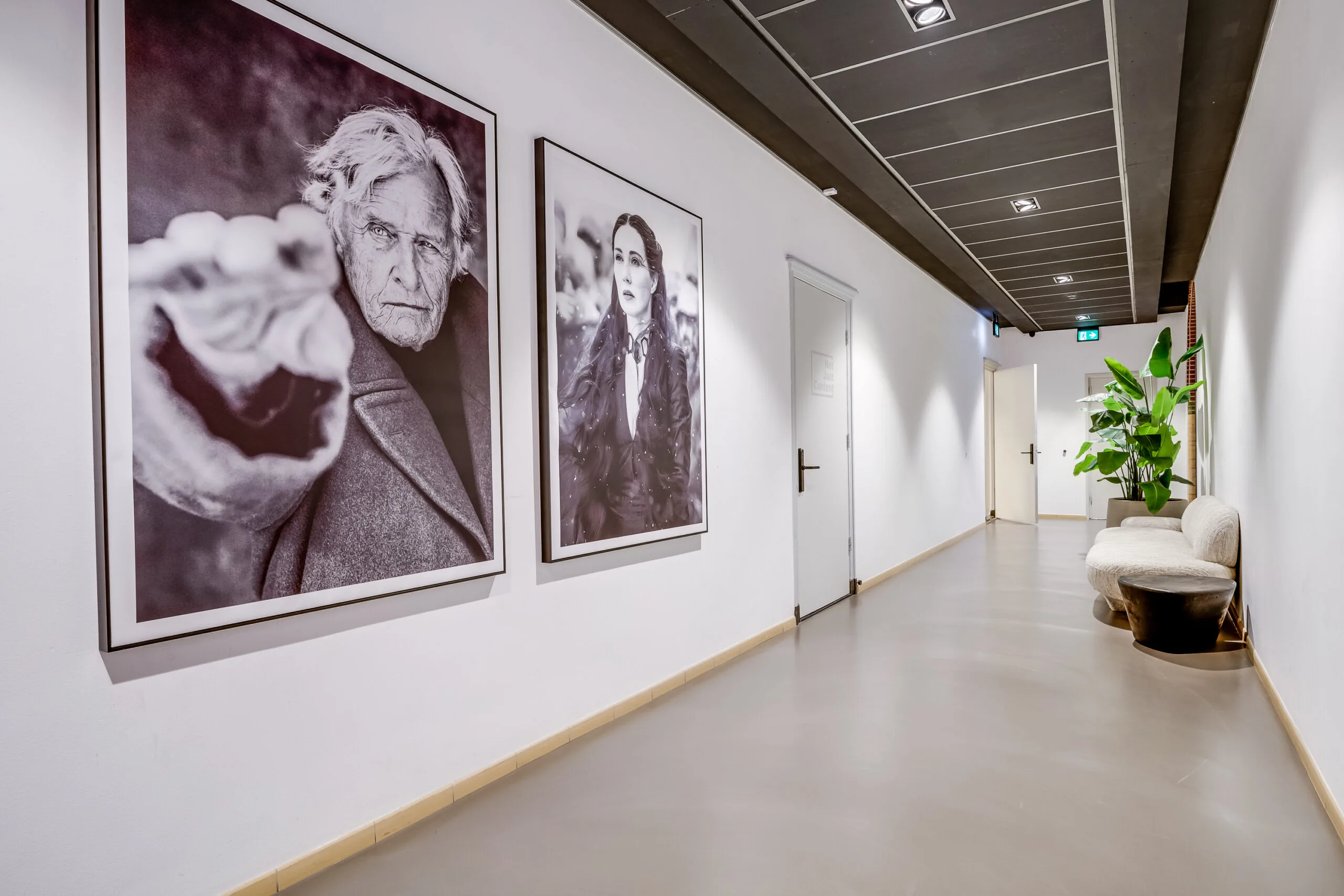 Modern hallway on Lage Naarderweg with large black-and-white portraits, minimalistic seating, and indoor plants.