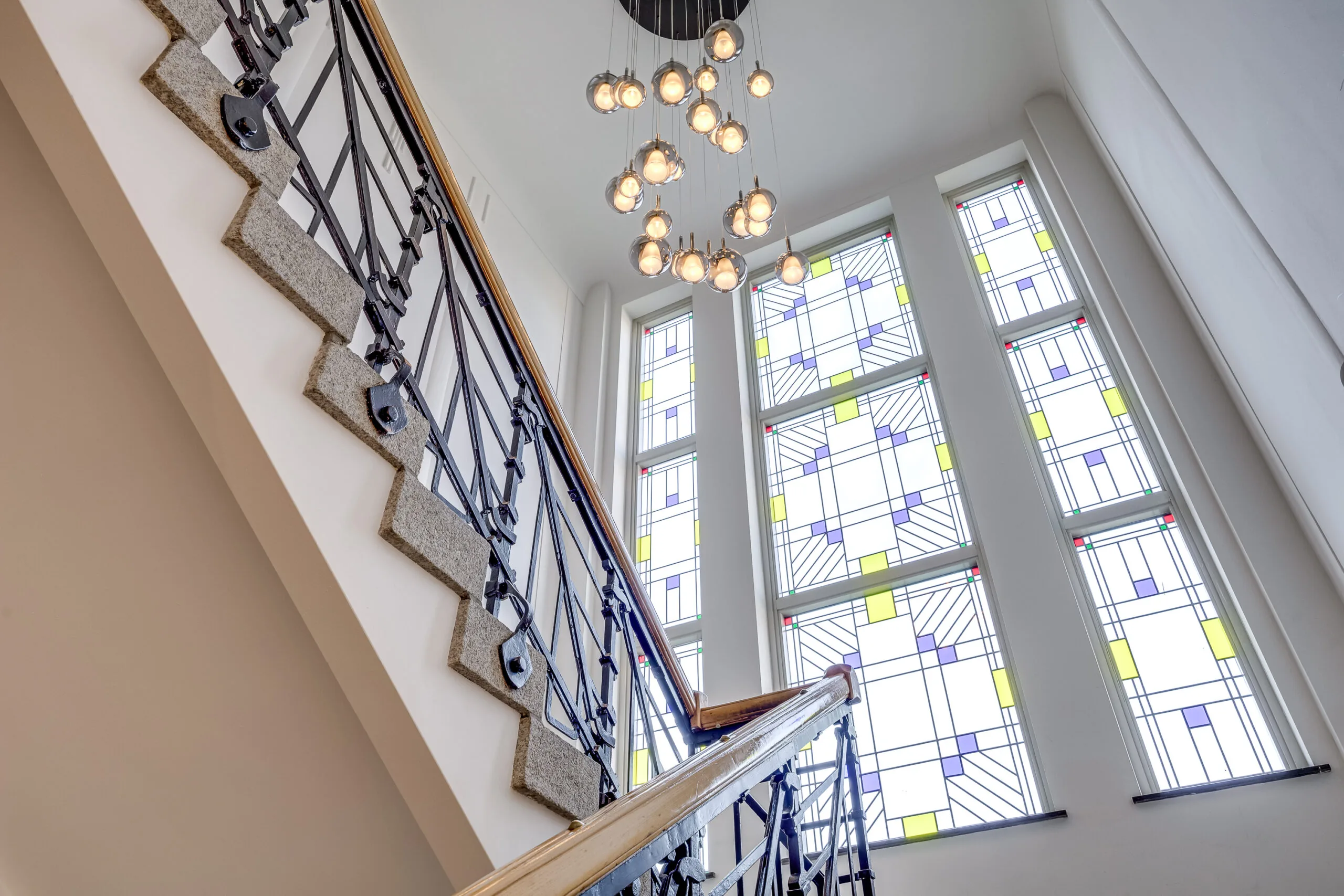 Stairwell with decorative stained-glass windows and a modern chandelier at Lage Naarderweg.