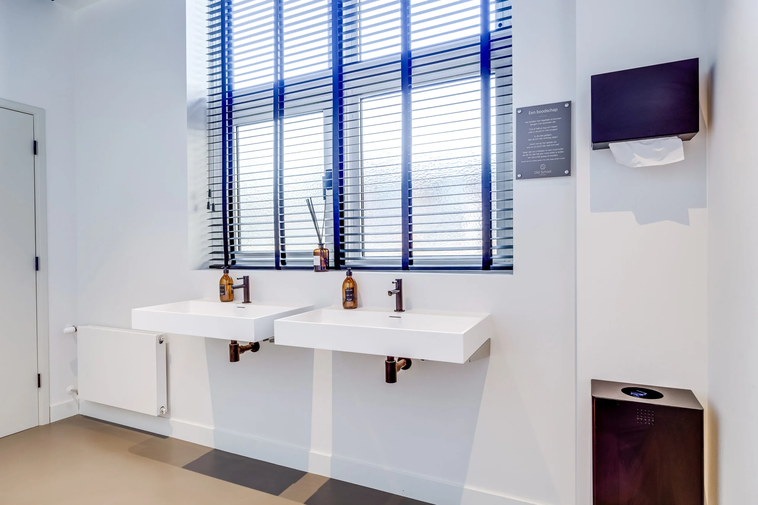 Modern restroom interior with two white sinks, black faucets, and large windows with horizontal blinds on Lage Naarderweg.
