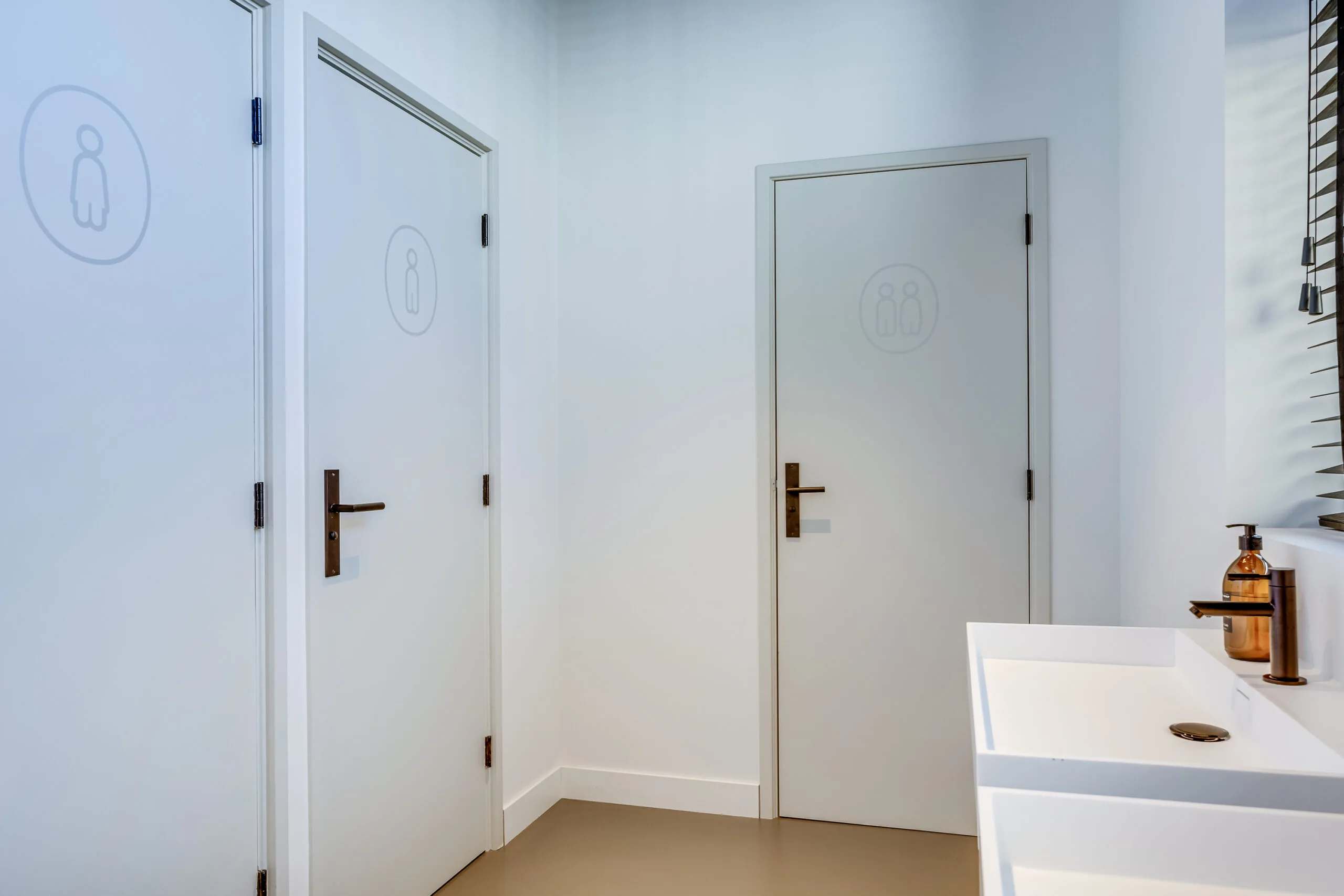 Modern public restroom area with three labeled doors for female, male, and unisex toilets, located on Lage Naarderweg.