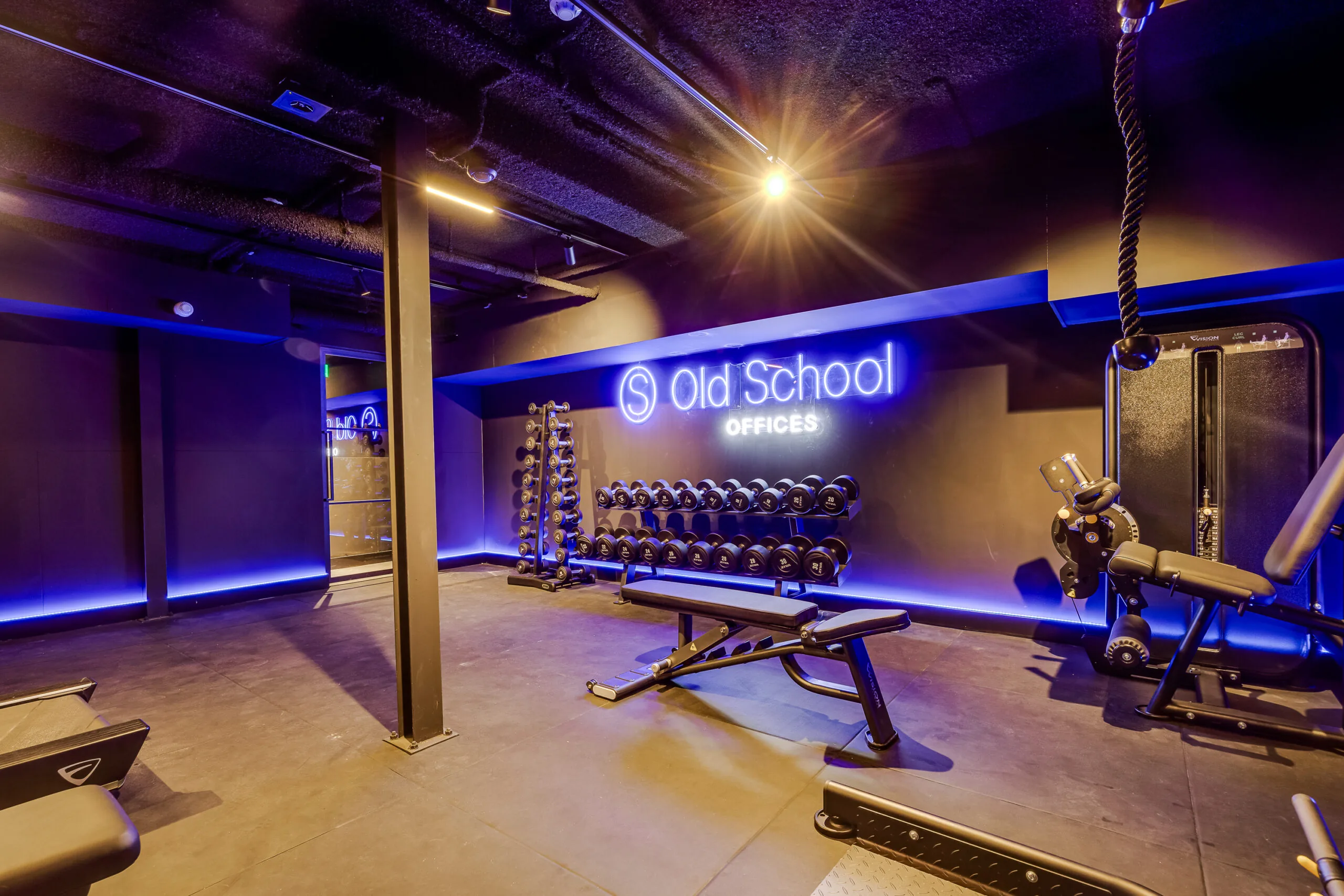 Modern gym space at Old School Offices with free weights, workout benches, and ambient blue lighting.