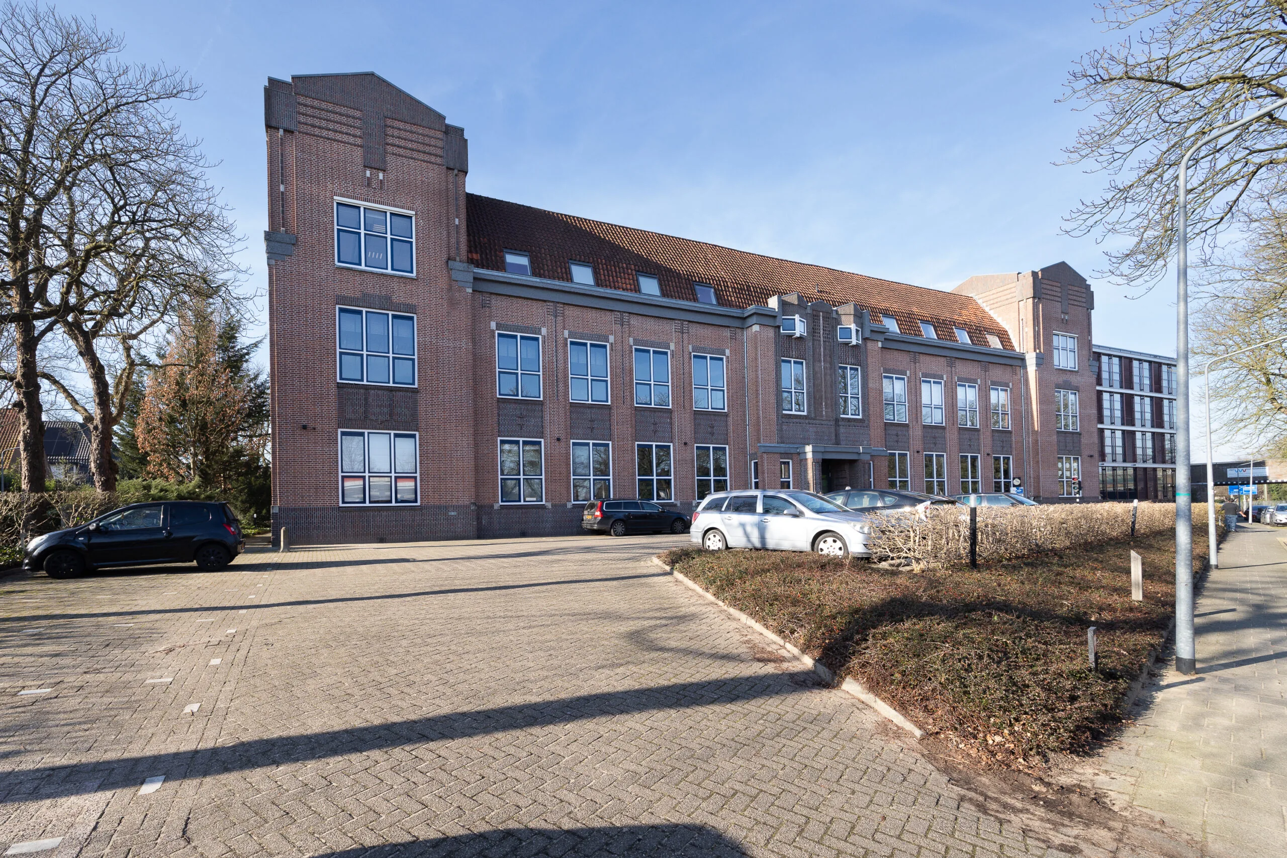 Brick office building on Lage Naarderweg with parked cars in front on a sunny day.