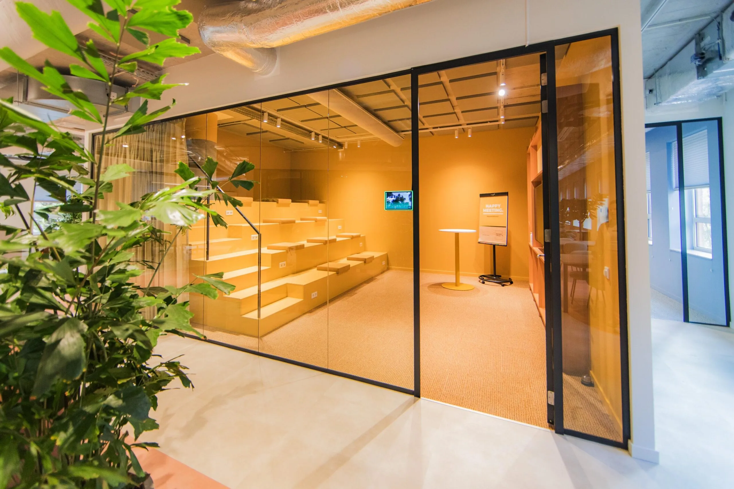 Modern glass meeting room at Hullenbergweg with yellow tiered seating and presentation setup.