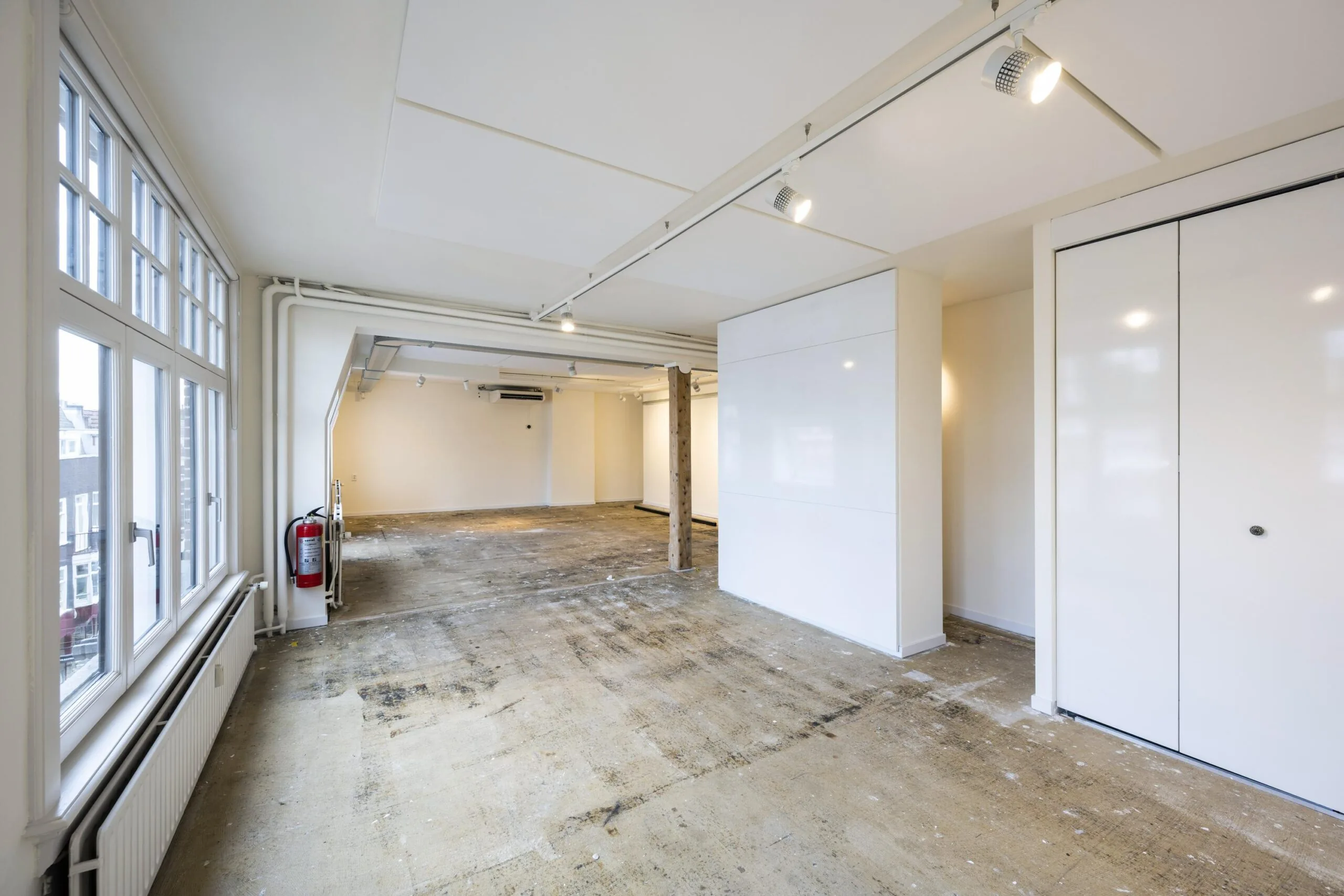 Leegstaand, licht studio- of winkelpand aan de Nieuwe Spiegelstraat met grote ramen en een onafgewerkte vloer.