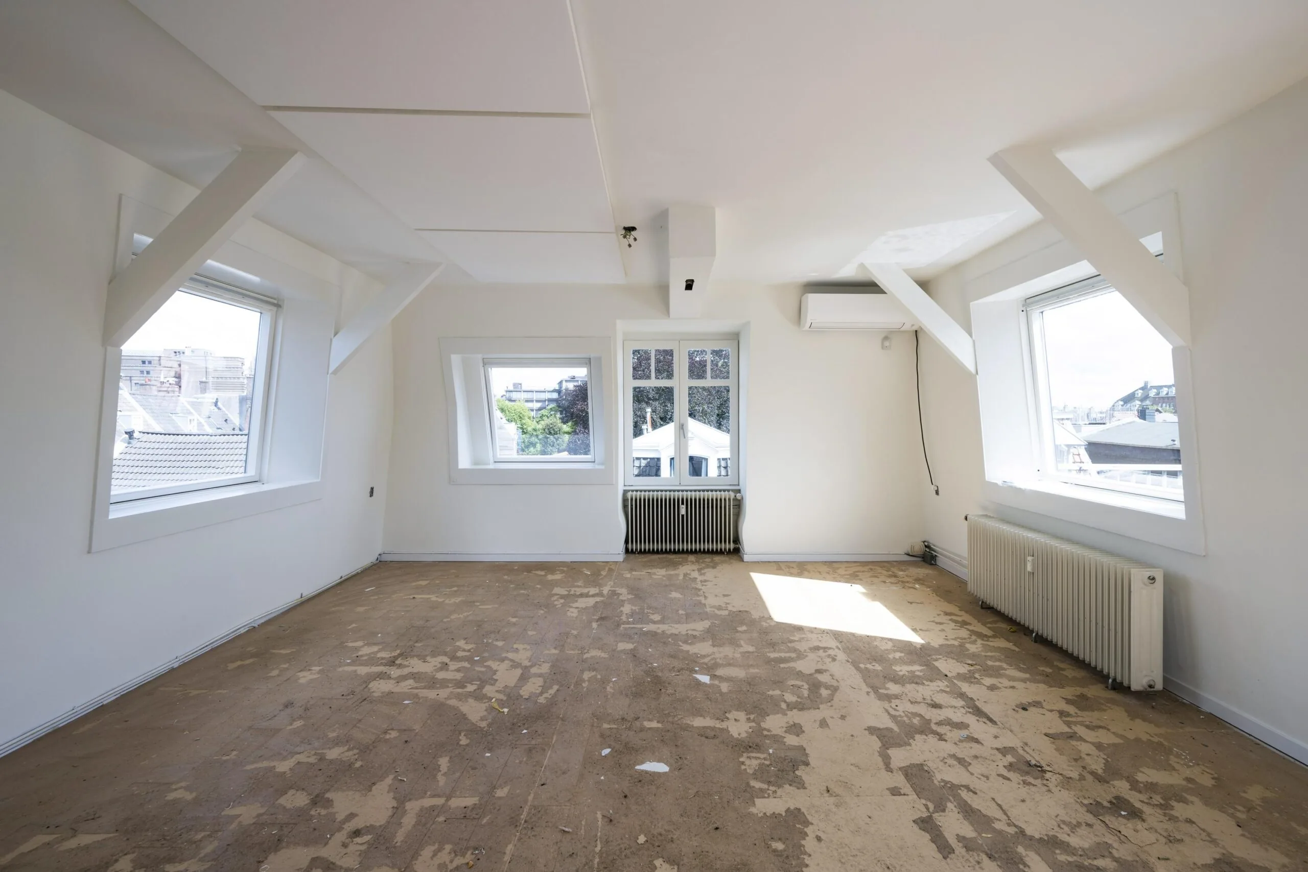 Lichte zolderkamer aan de Nieuwe Spiegelstraat met kale vloer, witte muren, schuine ramen en zicht op de stad.