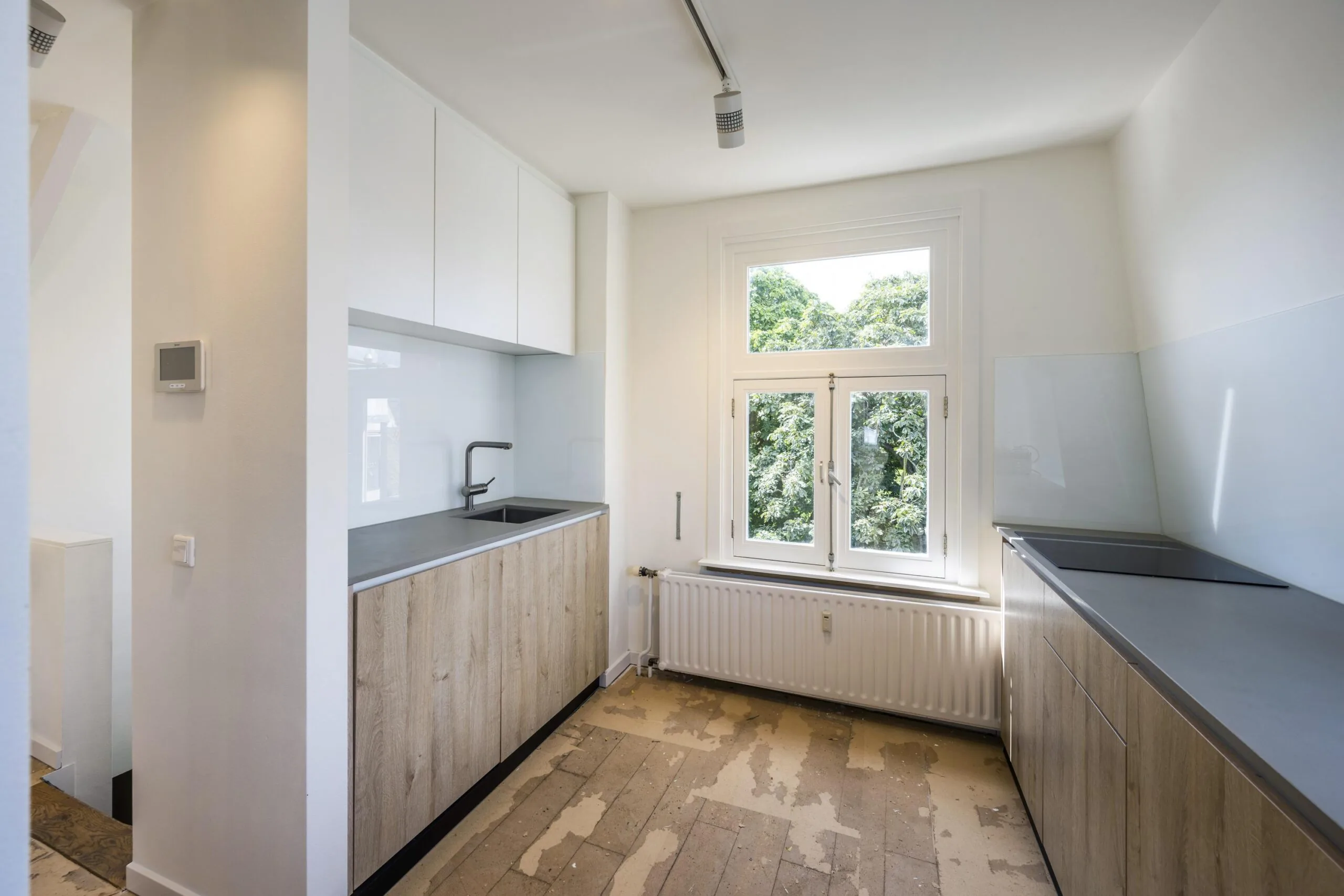 Moderne keuken aan de Nieuwe Spiegelstraat met houten keukenkasten, witte bovenkasten en uitzicht op groene bomen door een groot raam.
