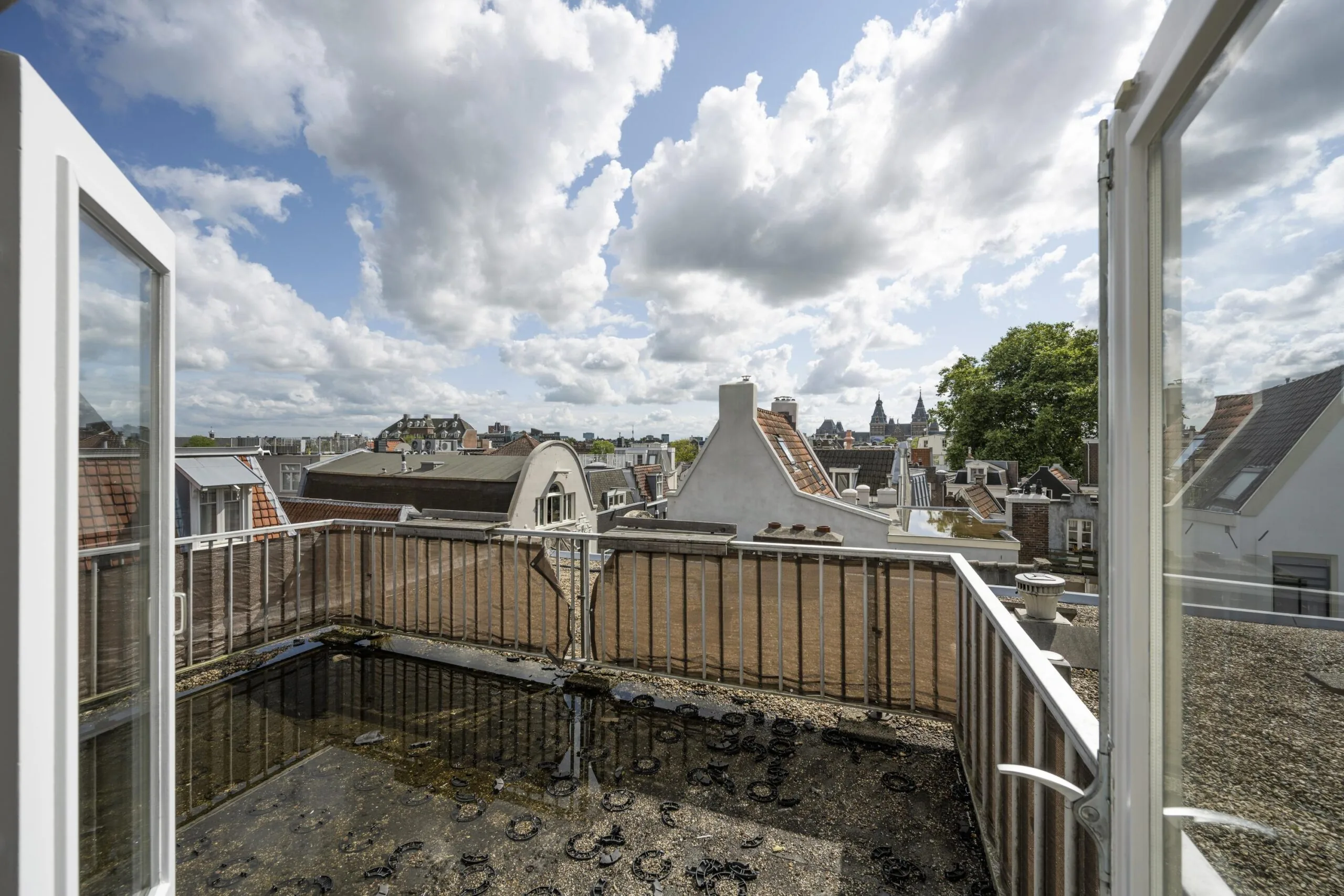 Uitzicht vanaf een dakterras in de Nieuwe Spiegelstraat met karakteristieke Amsterdamse daken en een deels bewolkte lucht.