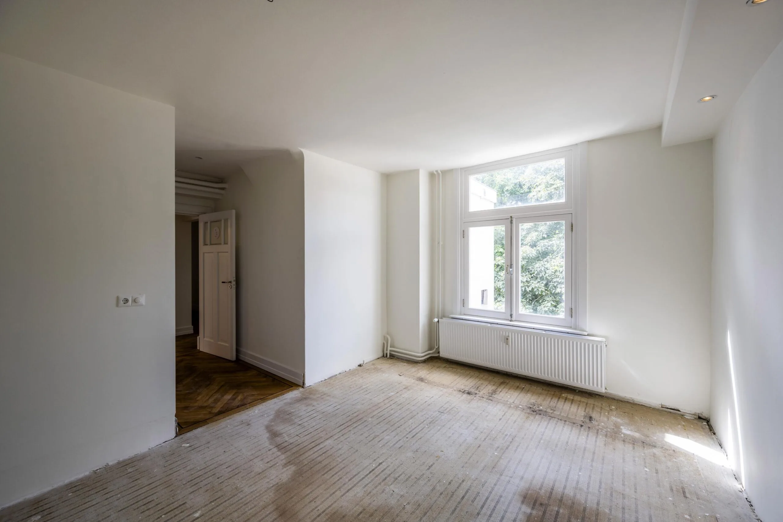Lege kamer in een woning aan de Nieuwe Spiegelstraat met witgeschilderde muren, een groot raam en een kale vloer.