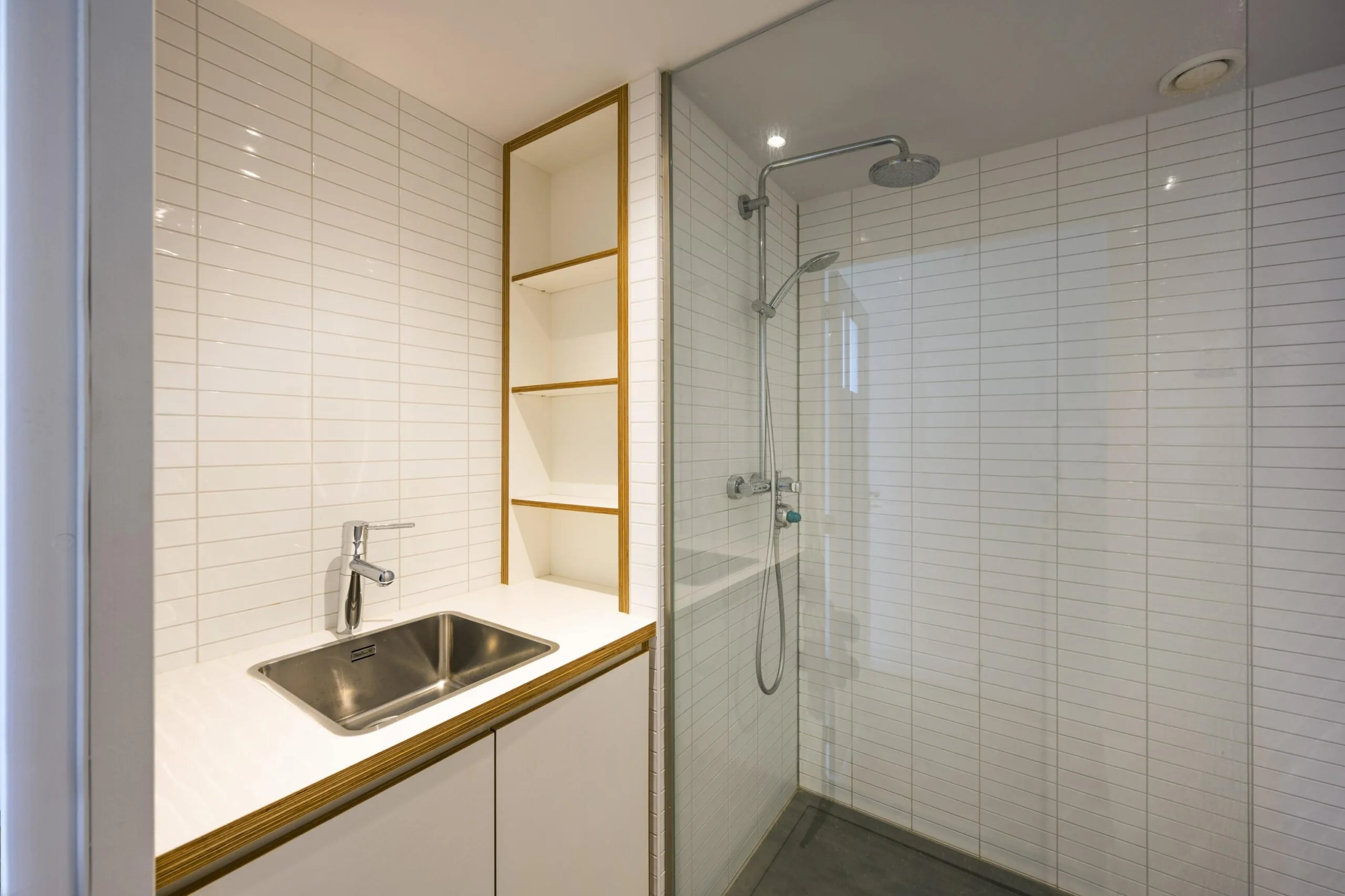 Moderne, wit betegelde badkamer met inloopdouche, wastafel en open wandkast in Nieuwe Spiegelstraat.