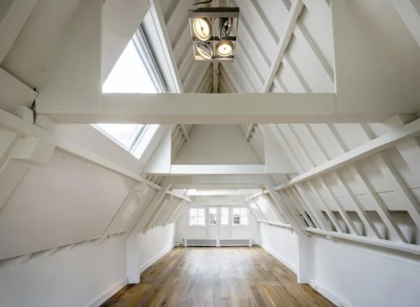 Zolderkamer met houten vloer, witte balken en grote dakramen aan de Nieuwe Spiegelstraat.
