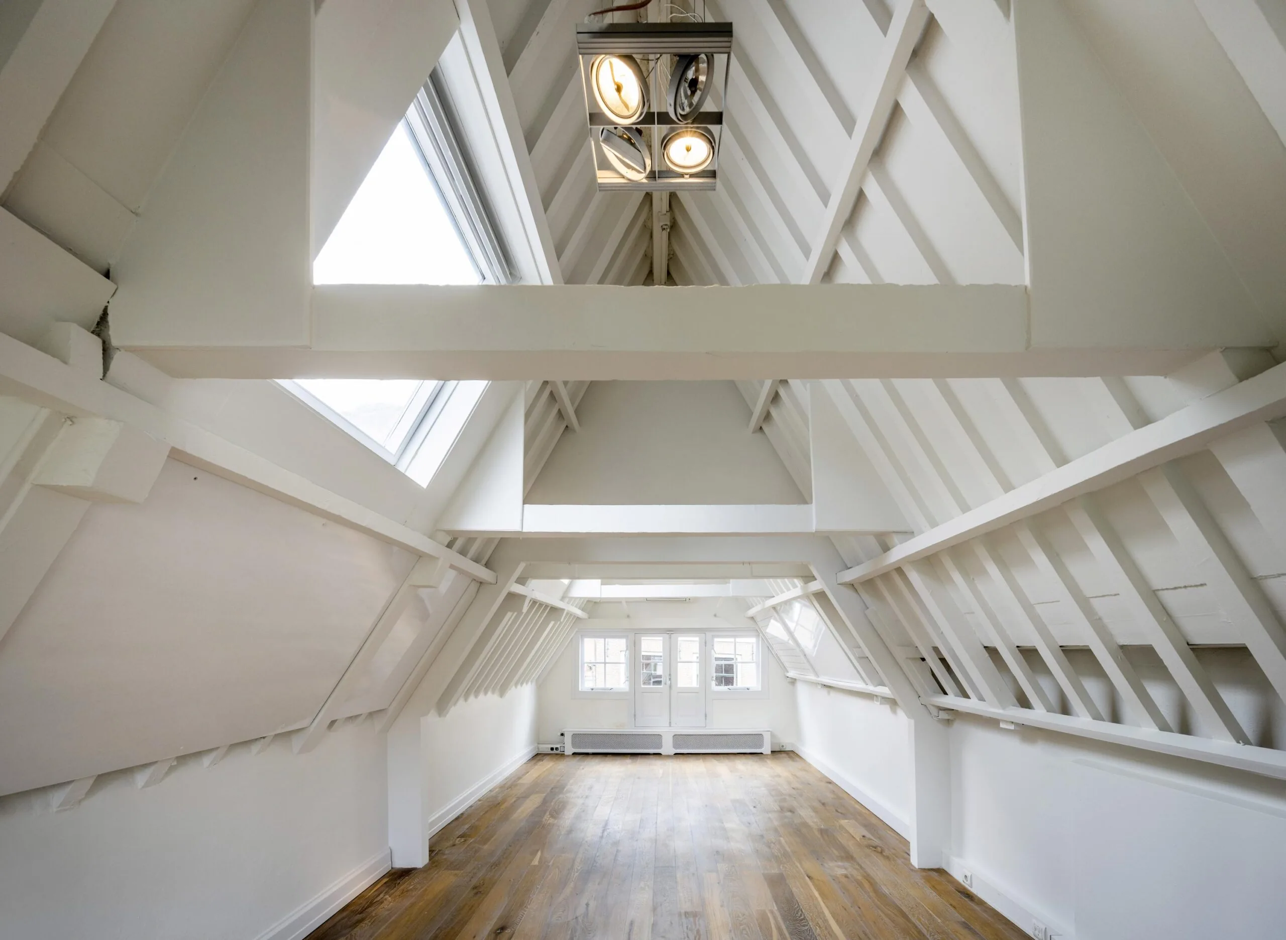 Zolderkamer met houten vloer, witte balken en grote dakramen aan de Nieuwe Spiegelstraat.