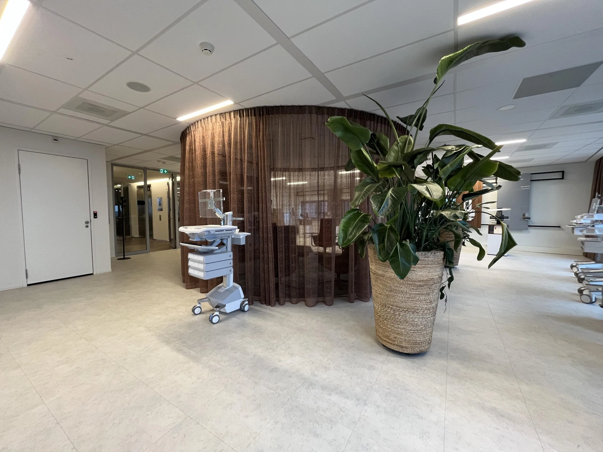 Moderne ziekenhuisruimte aan de Stationsstraat met medische apparatuur, een ronde gordijnruimte en een grote kamerplant.