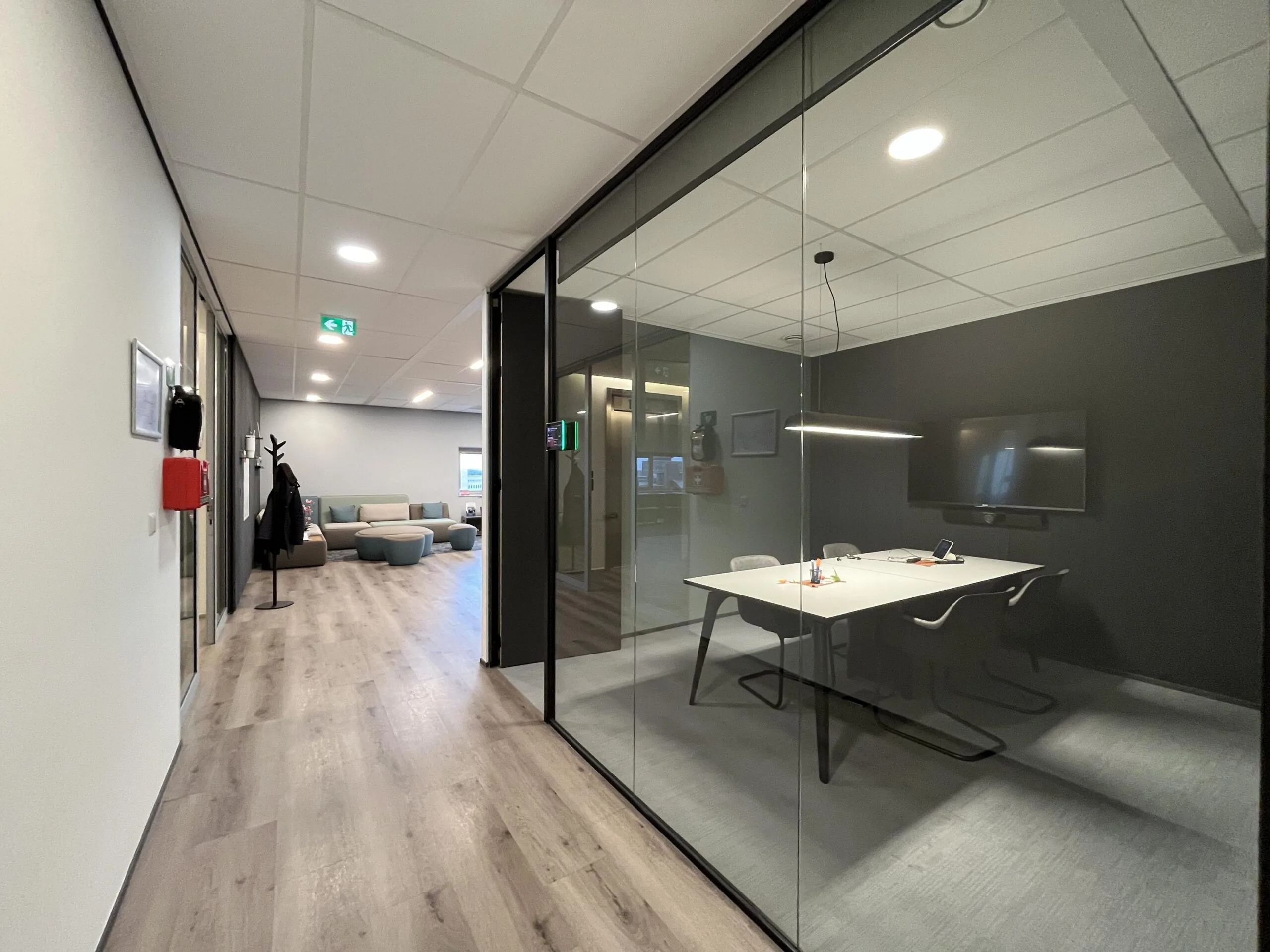 Kantoorinterieur met glazen vergaderruimte, gang en zithoek in een modern bedrijfsgebouw aan de Stationsstraat.