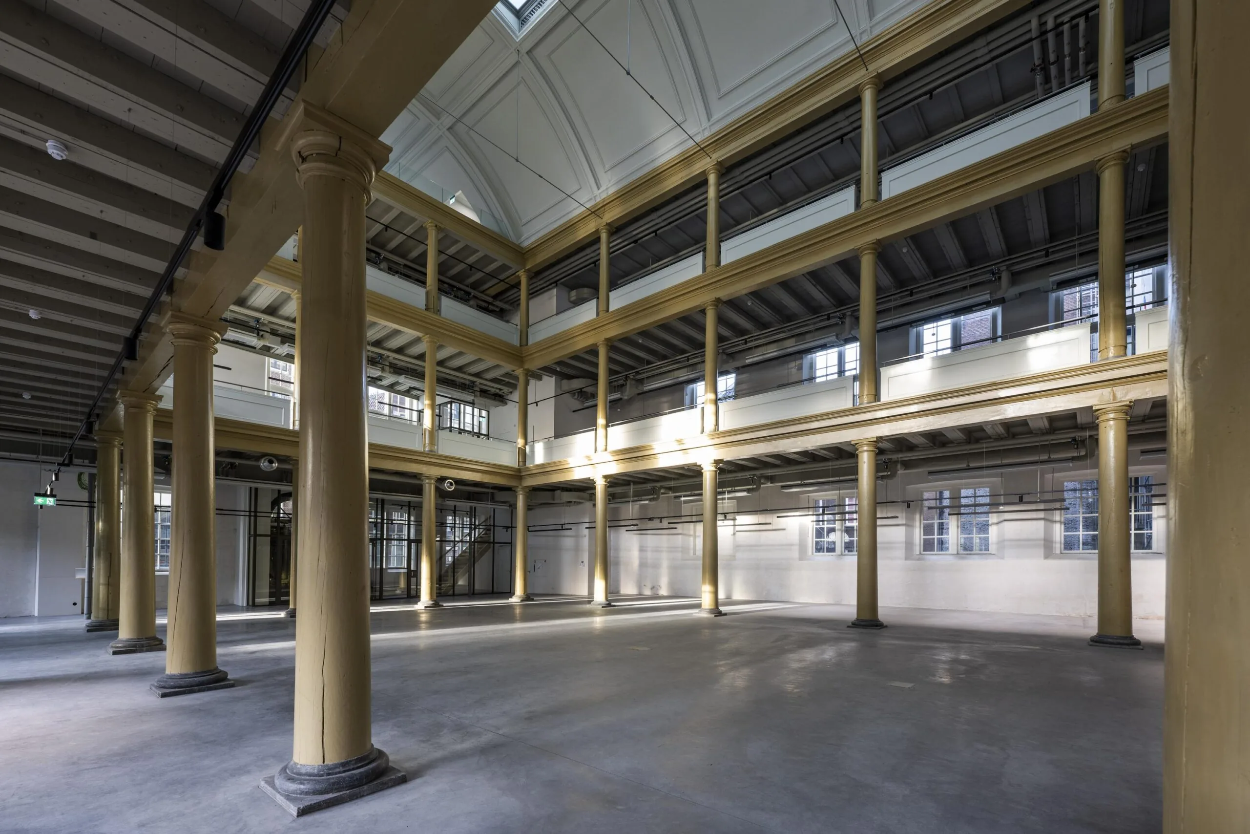 Interieur van een ruim, leeg en licht industrieel pand aan de Kloveniersburgwal met hoge plafonds en gele zuilen.