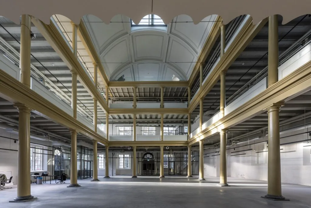 Licht en ruim atrium van het historische pand aan de Kloveniersburgwal met hoge plafonds, glazen dak en glazen wanden.