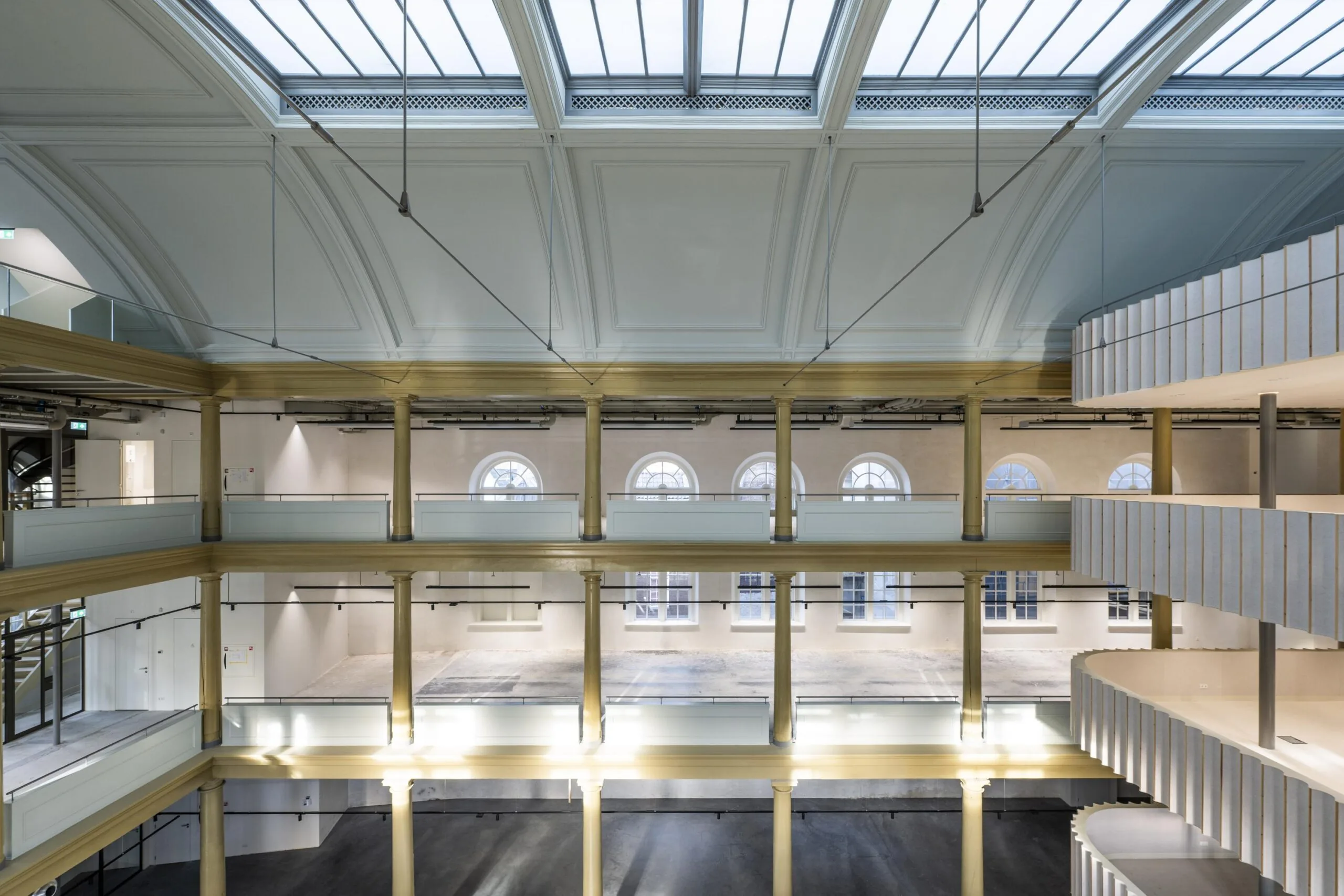 Licht atrium van het gerenoveerde pand aan de Kloveniersburgwal met glazen dak, klassieke zuilen en moderne balustrades.