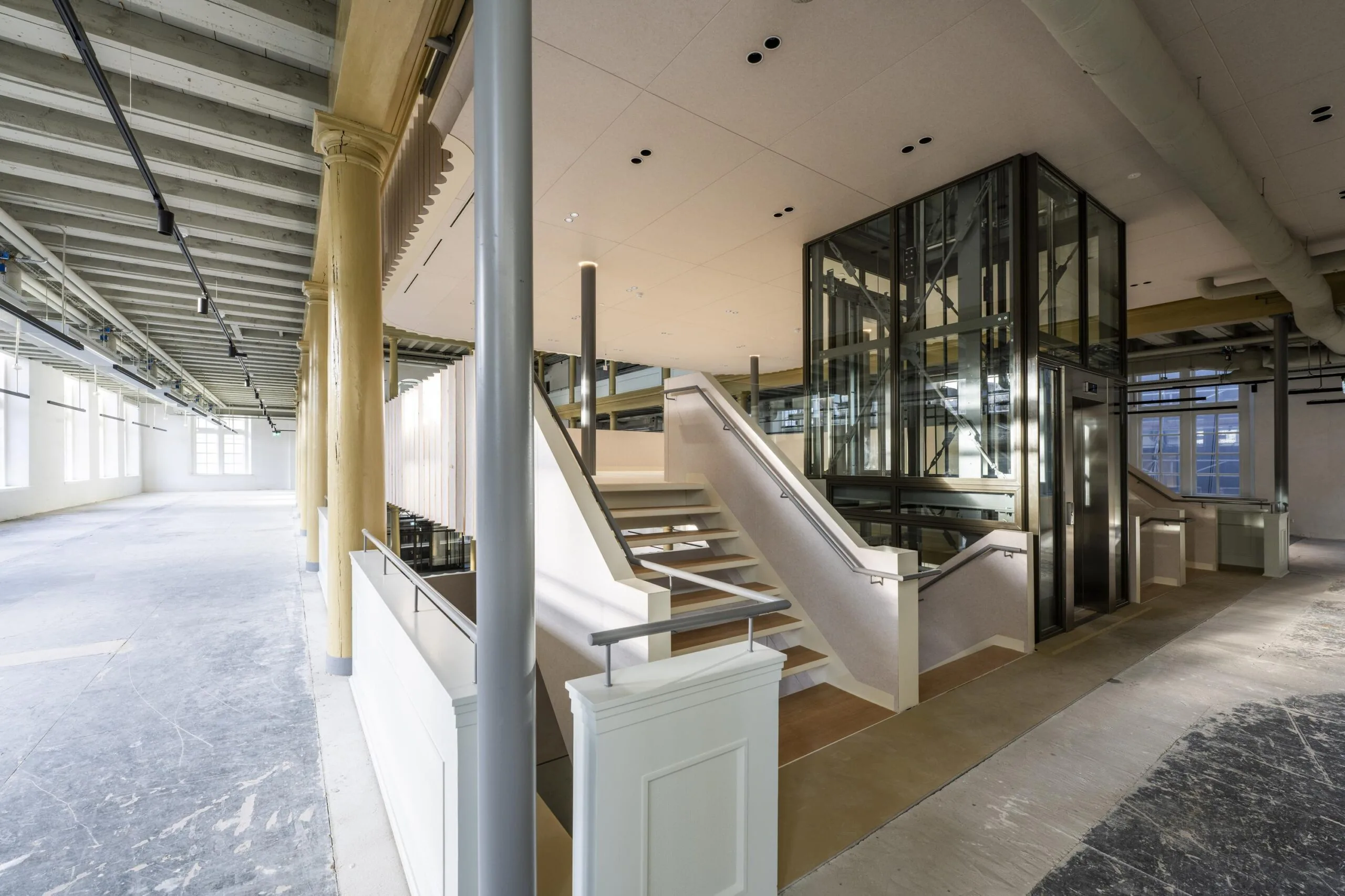 Moderne gerenoveerde binnenruimte aan de Kloveniersburgwal met glazen lift, trap en zichtbare plafondconstructie.