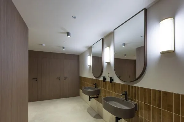 Moderne openbare toiletruimte met houten deuren, twee wastafels en grote spiegels aan de muur.