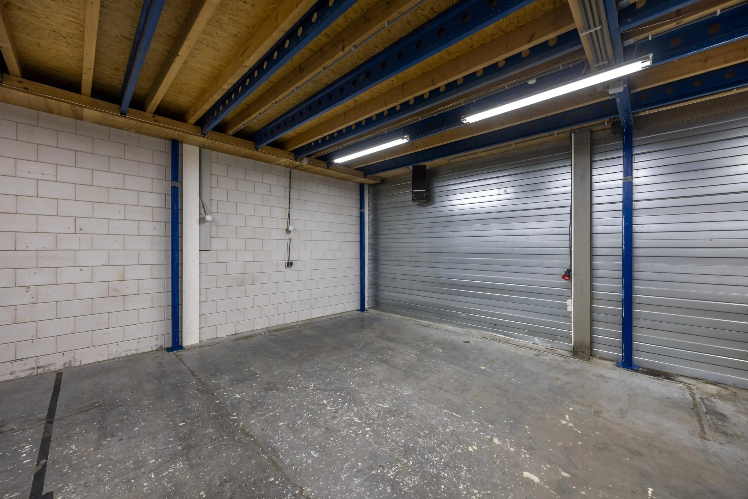 Lege bedrijfshal met betonnen vloer, witte bakstenen muur en metalen roldeur aan de Tennesseedreef.