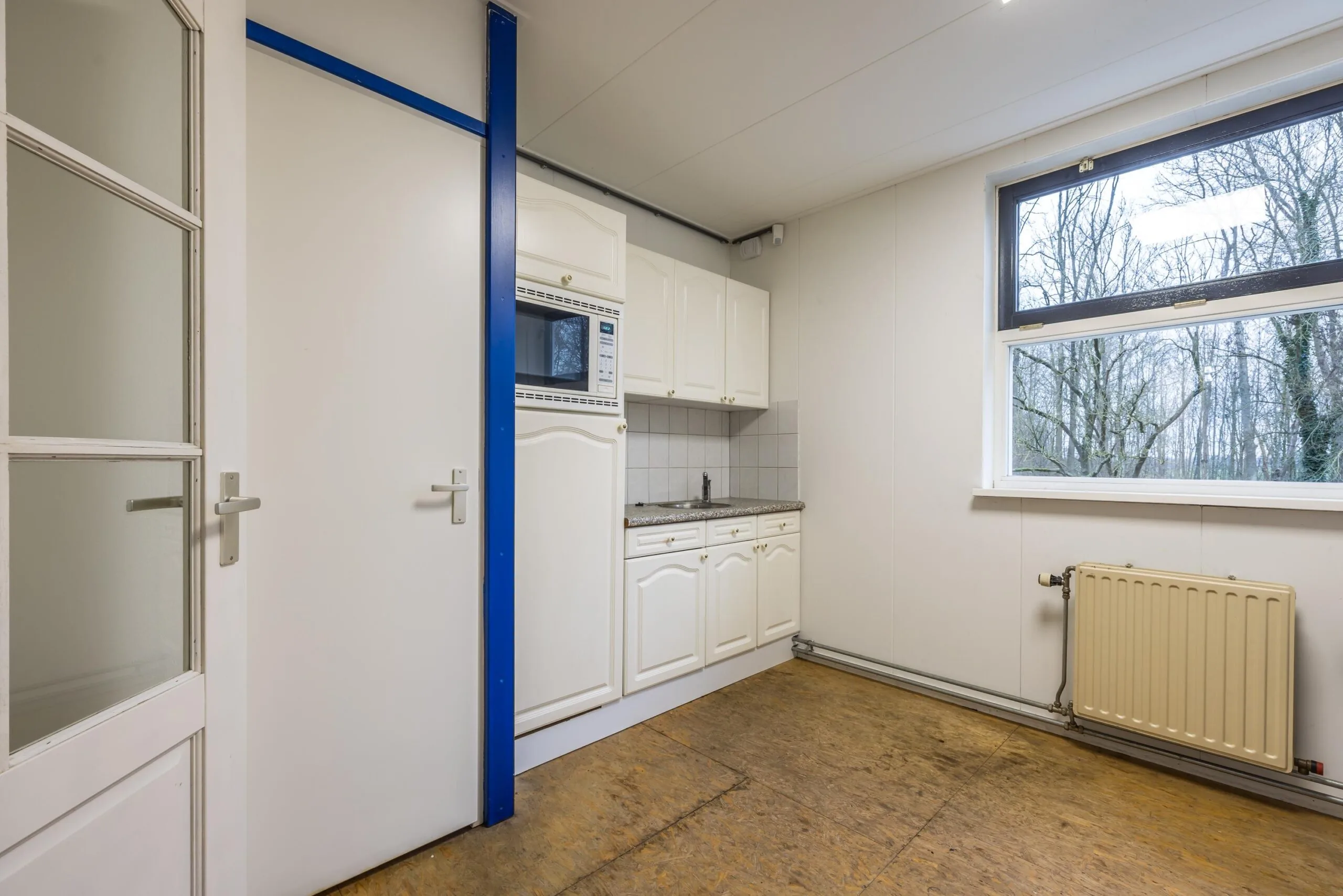 Kleine eenvoudige keuken met witte kasten, een magnetron en een groot raam aan de Tennesseedreef.