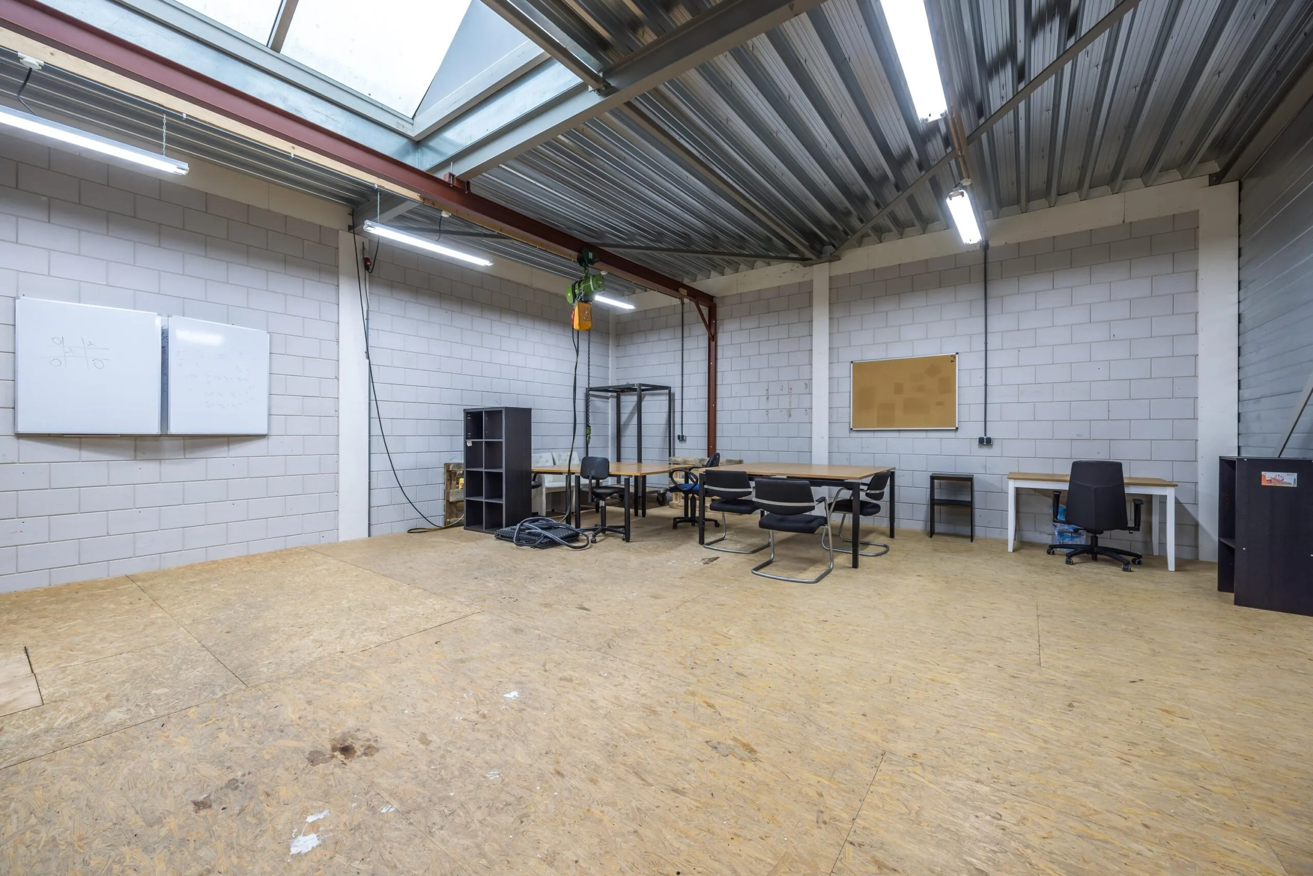 Ruimte aan de Tennesseedreef met bureaus, stoelen, whiteboards en industriële inrichting onder een metalen dak.