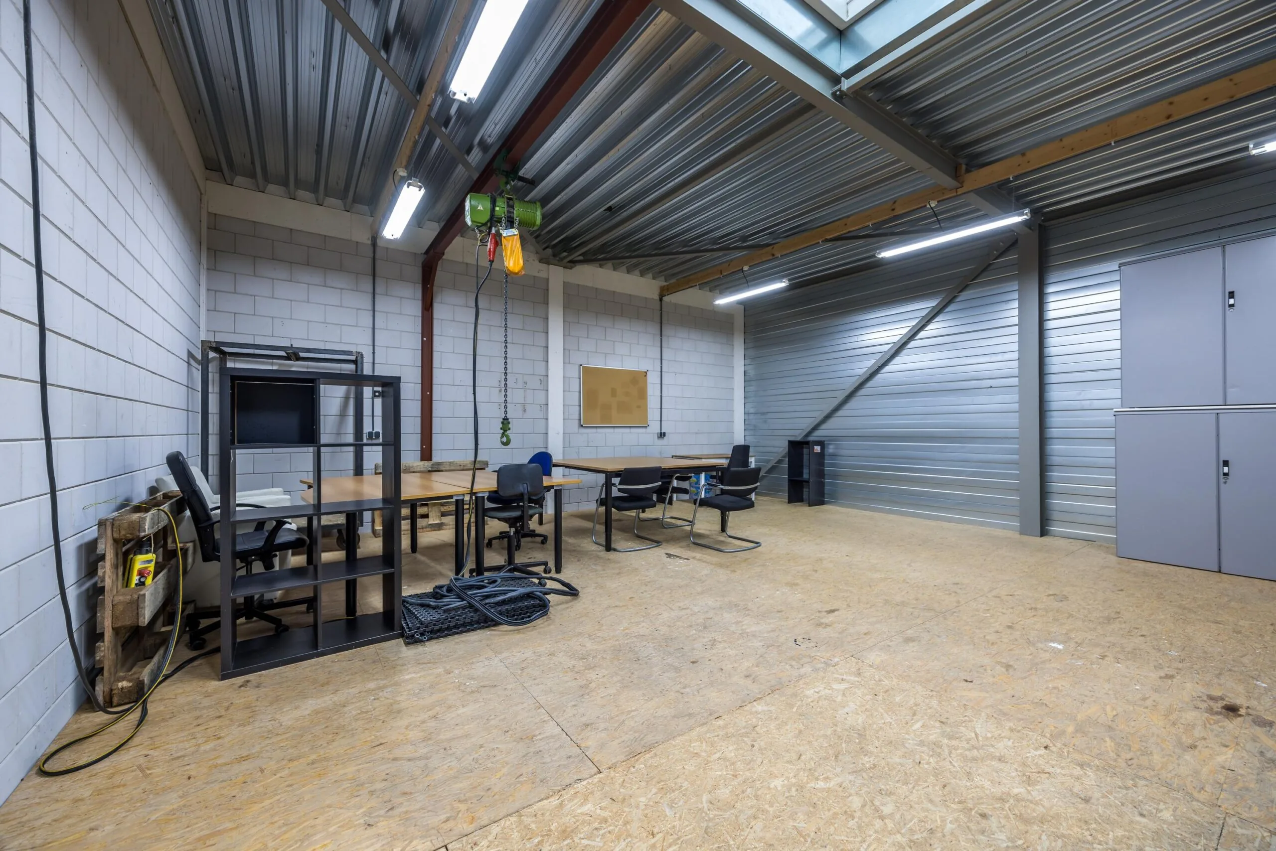 Een industriële werkruimte aan de Tennesseedreef met bureaus, stoelen, metalen kasten en een hijswerktuig aan het plafond.