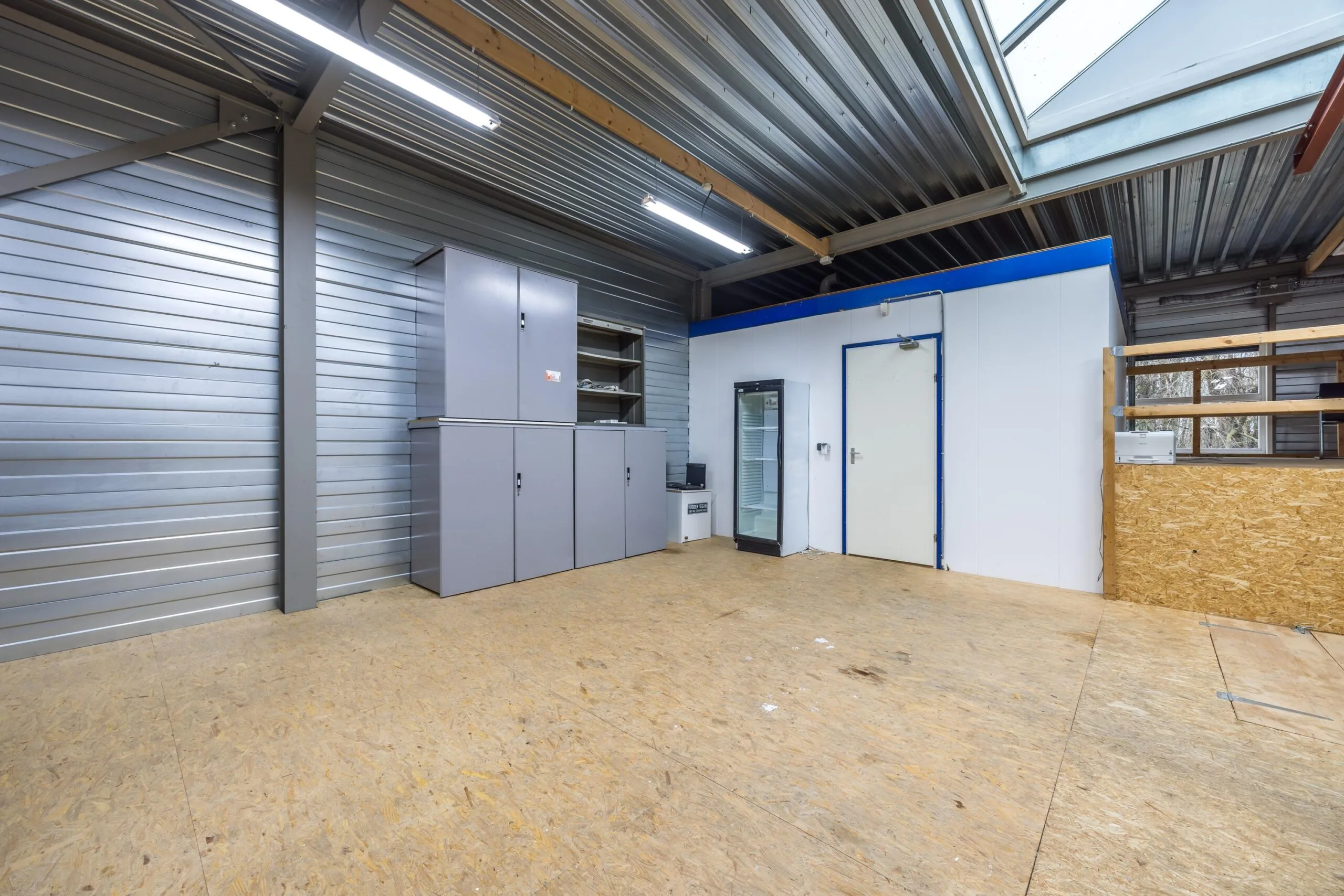 Industrieel ingerichte ruimte aan de Tennesseedreef met metalen kasten, een koelkast, houten vloer en metalen plafond met dakraam.