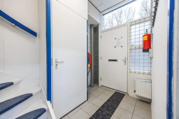 Ingang van een trappenhuis op de Tennesseedreef met een witte deur, brandslanghaspel en brandblusser.