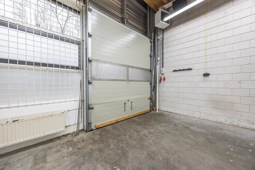 Interieur van een lege bedrijfsruimte aan de Tennesseedreef met een gesloten roldeur, betonnen vloer en witte bakstenen muren.