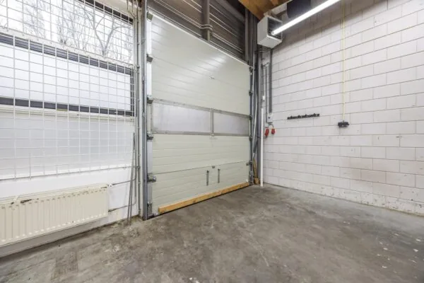 Interieur van een lege bedrijfsruimte aan de Tennesseedreef met een gesloten roldeur, betonnen vloer en witte bakstenen muren.