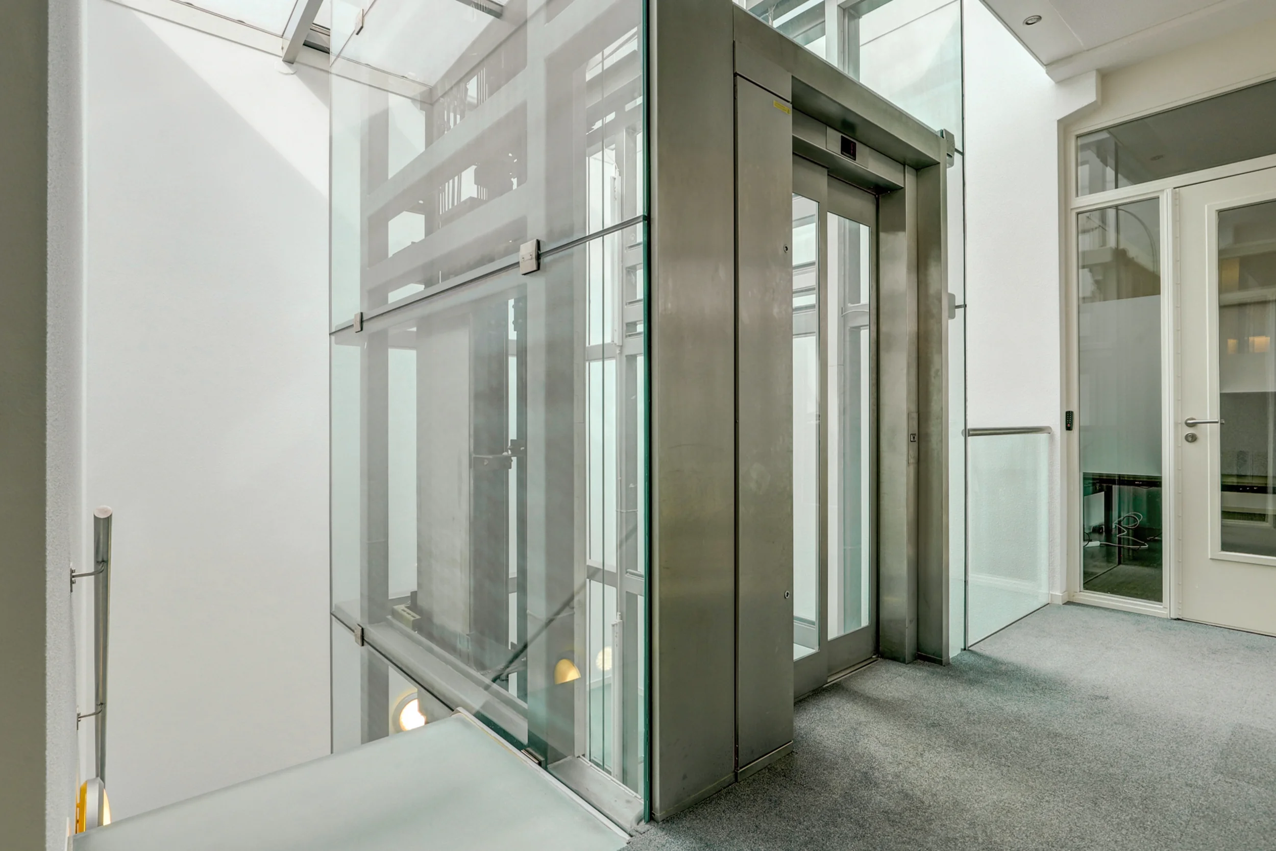 Glazen lift met metalen frame in een modern, licht trappenhuis aan de New Yorkstraat.
