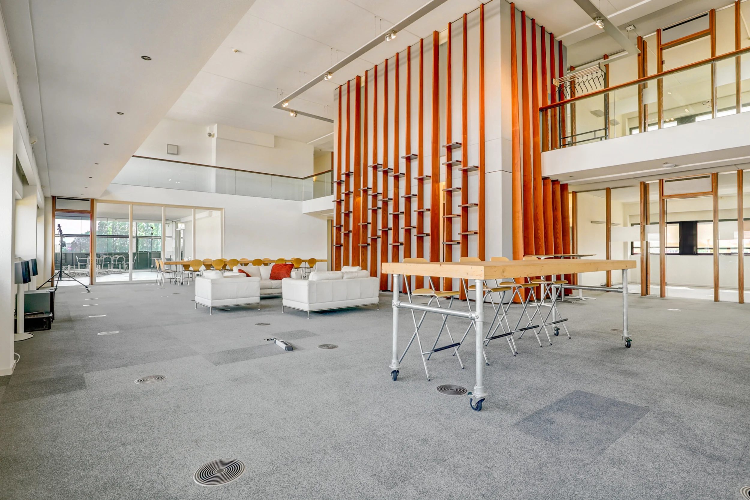 Ruime en moderne kantoorruimte met glazen balustrade, houten designelementen en een loungegedeelte met witte banken.