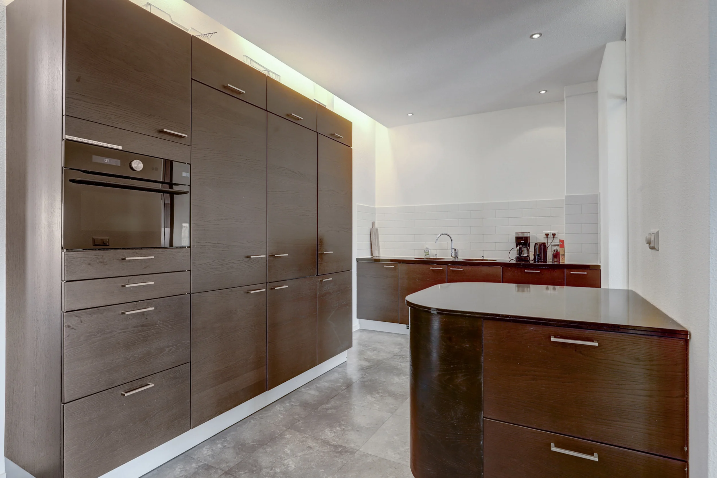 Moderne keuken met donkerhouten kasten, ingebouwde oven en een licht betegelde achterwand.
