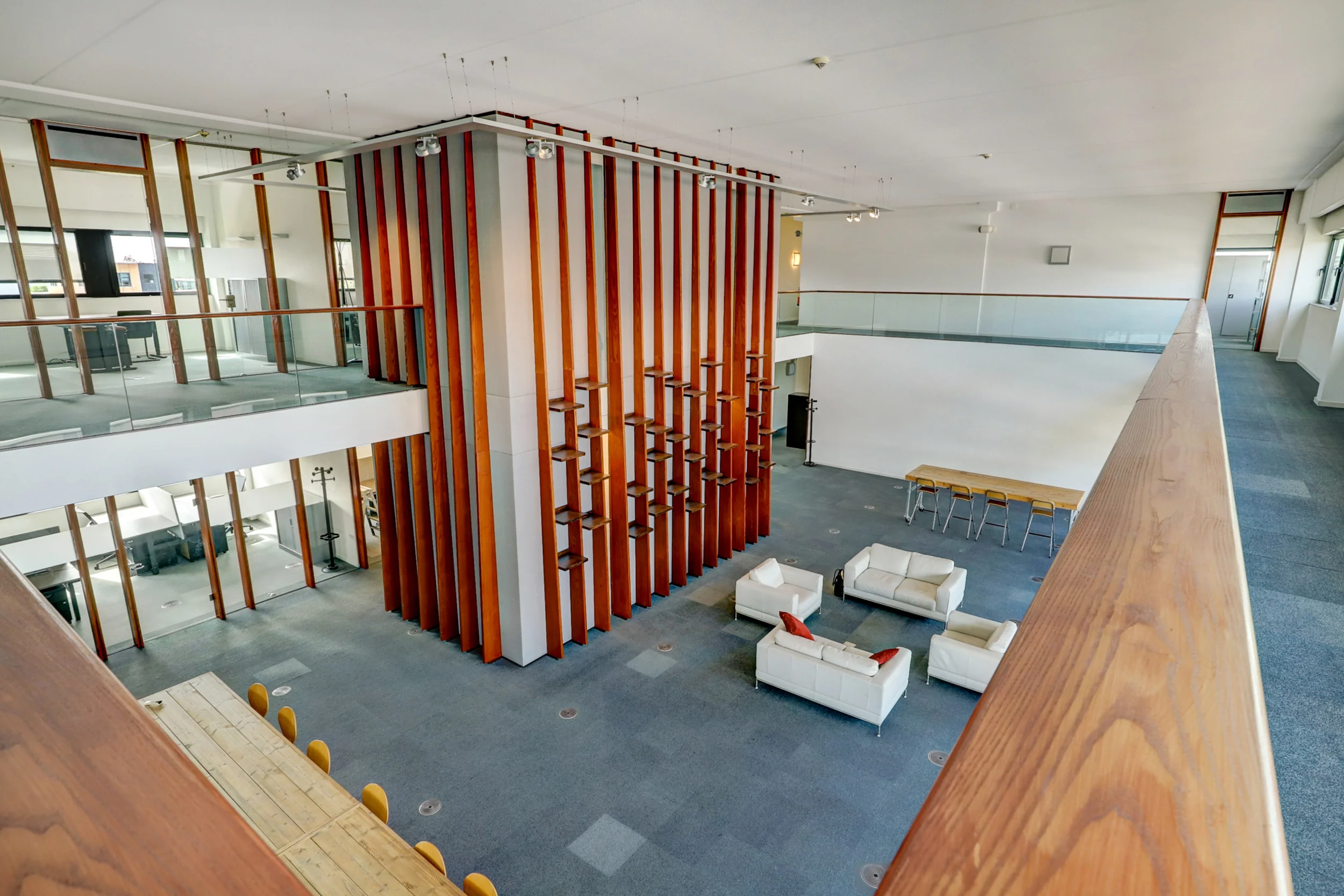 Modern kantoorinterieur met open verdiepingen, een hoge houten structuur en lichte zithoeken.