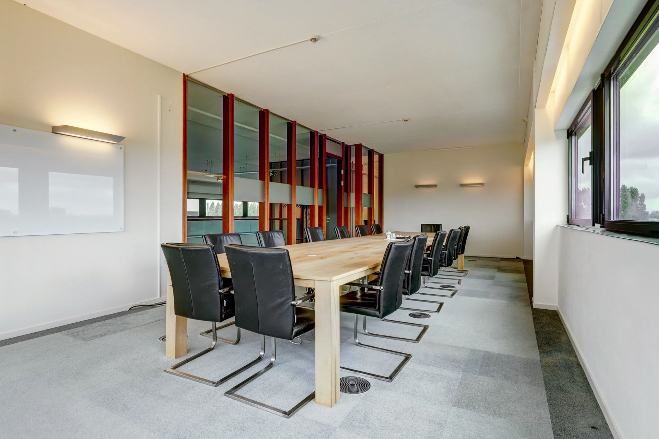 Moderne vergaderruimte met lange houten tafel, zwarte stoelen en grote ramen aan de rechterzijde.
