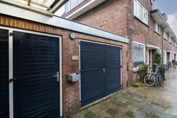 Vooraanzicht van een bakstenen woning aan de Balderikstraat met donkerblauwe garagedeuren en enkele fietsen op de stoep.