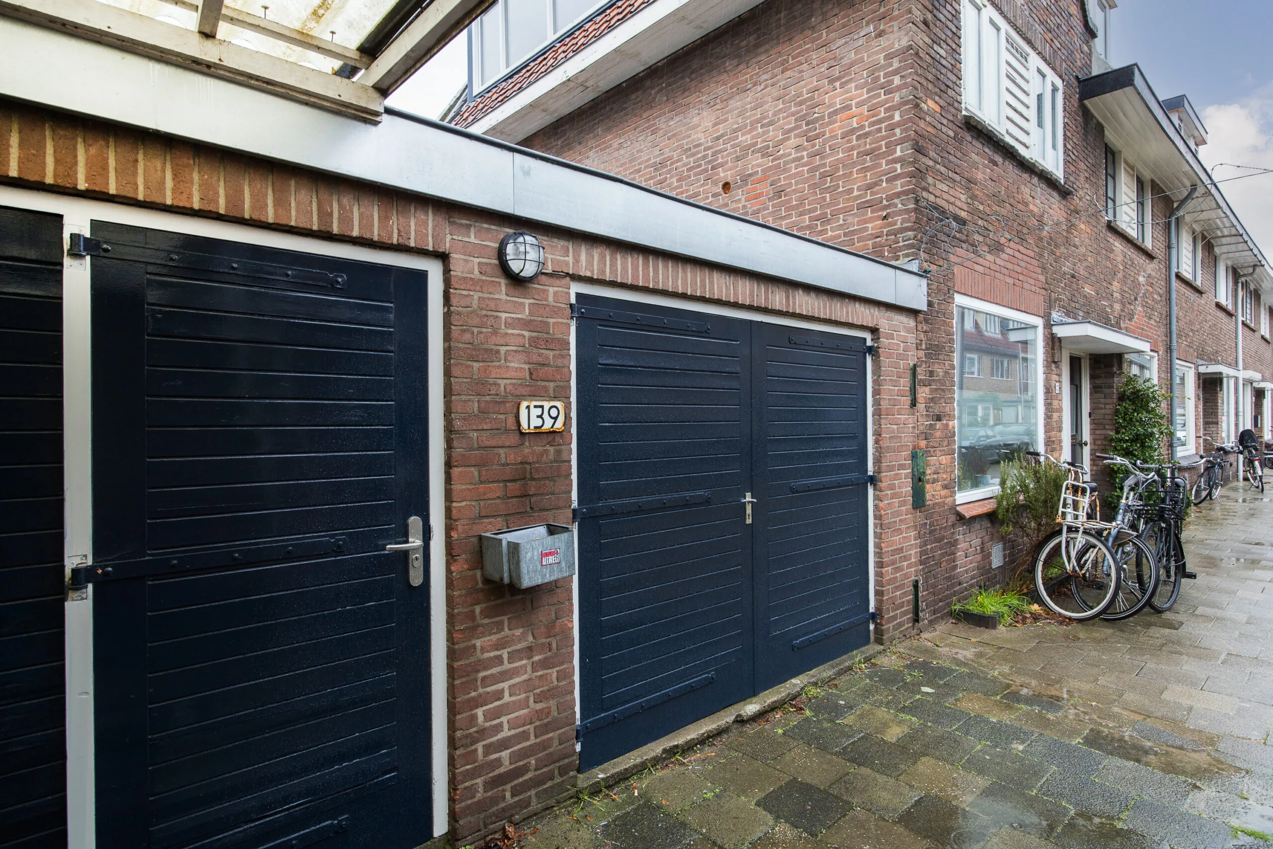 Vooraanzicht van een bakstenen woning aan de Balderikstraat met donkerblauwe garagedeuren en enkele fietsen op de stoep.