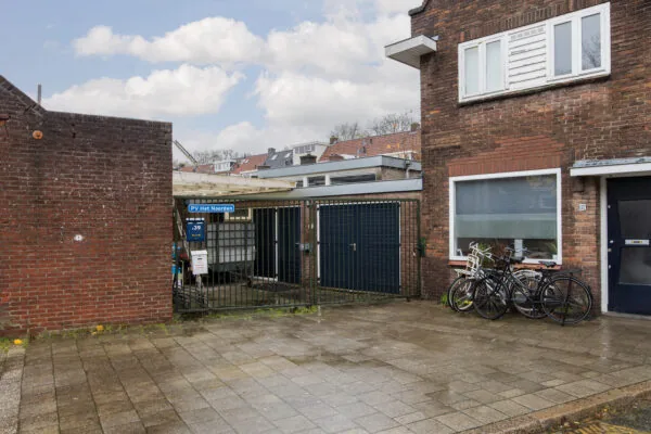 Ingang met hek van PV Het Noorden aan de Balderikstraat, naast een woonhuis met geparkeerde fietsen op de stoep.