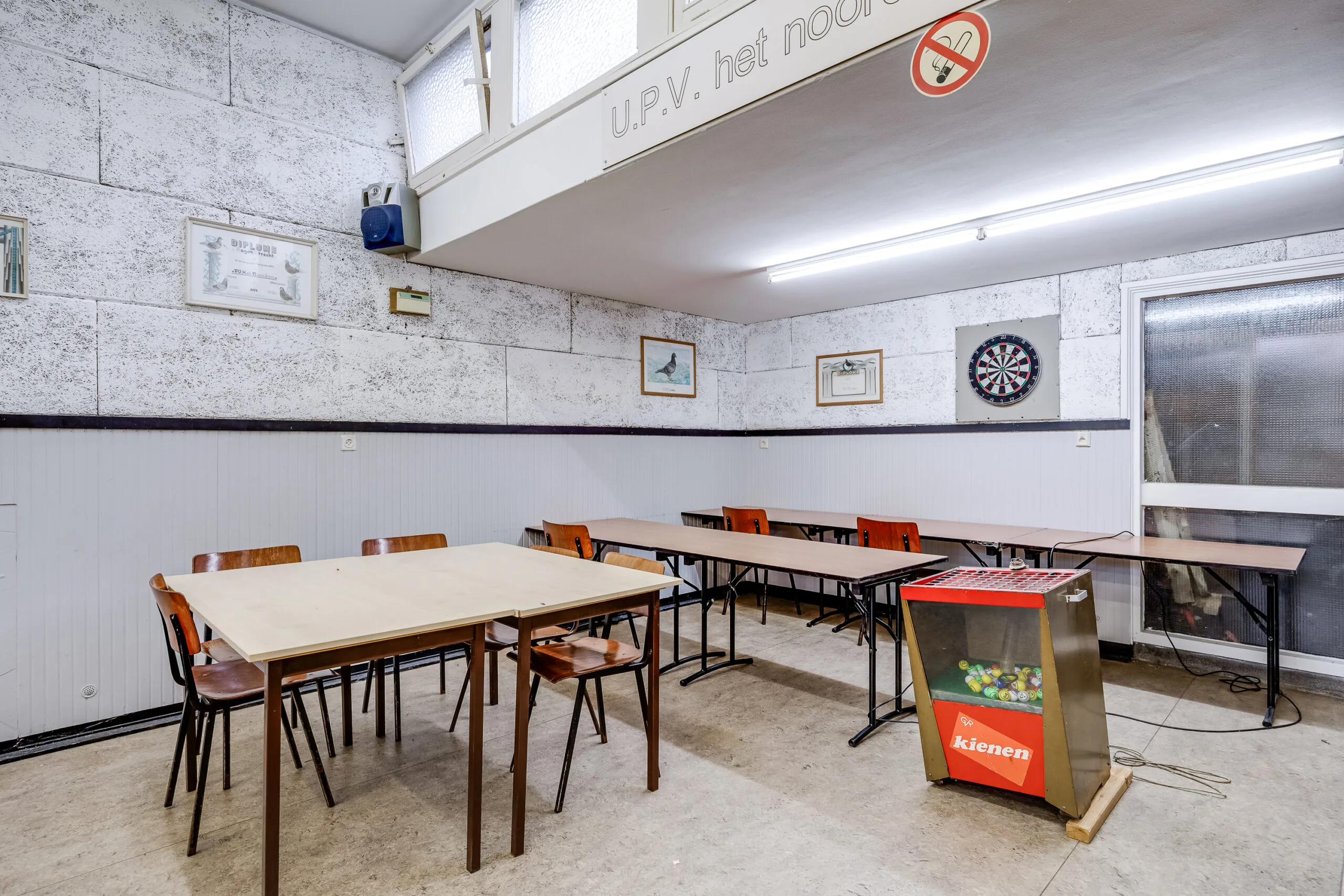 Ingerichte gemeenschapsruimte in de Balderikstraat met tafels, stoelen, een dartbord en een kienmachine.