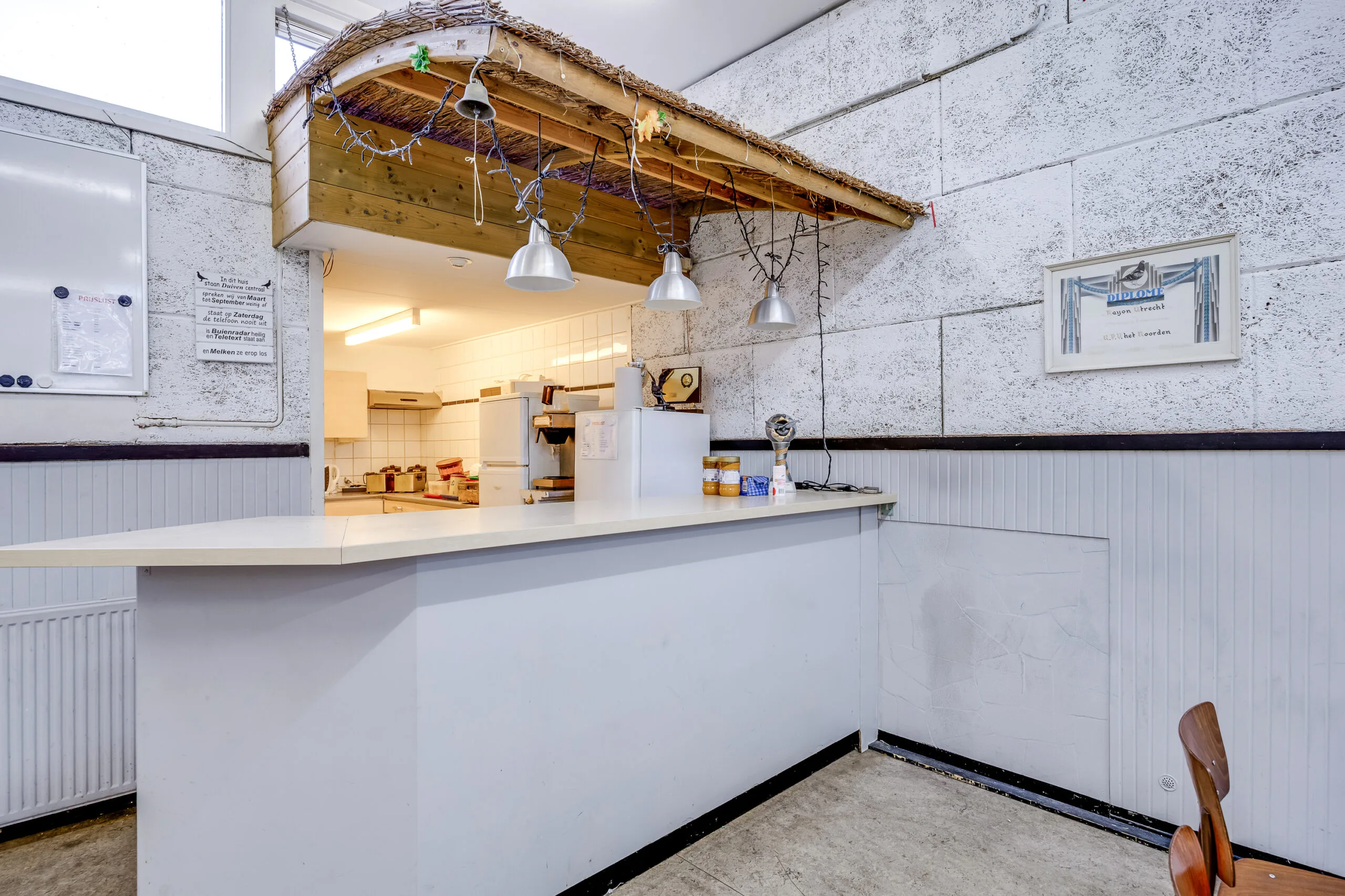 Witte balie met hanglampen en een open keuken in een kantine aan de Balderikstraat.