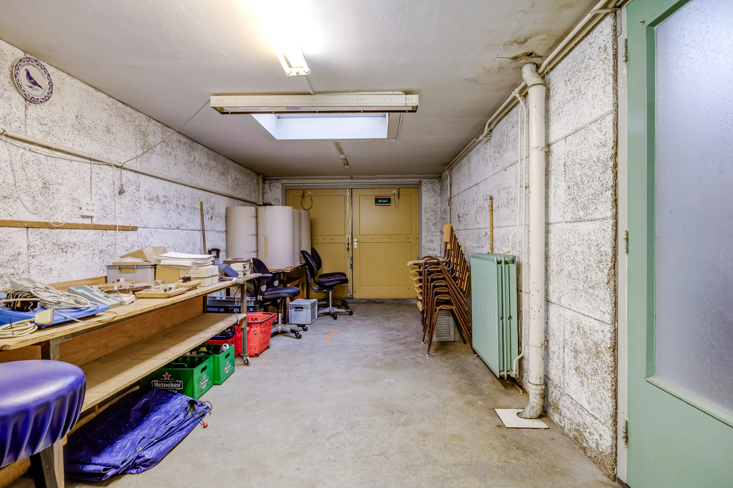 Opberg- en klusruimte in de Balderikstraat met werkbank, stapelstoelen en kantoorstoelen.
