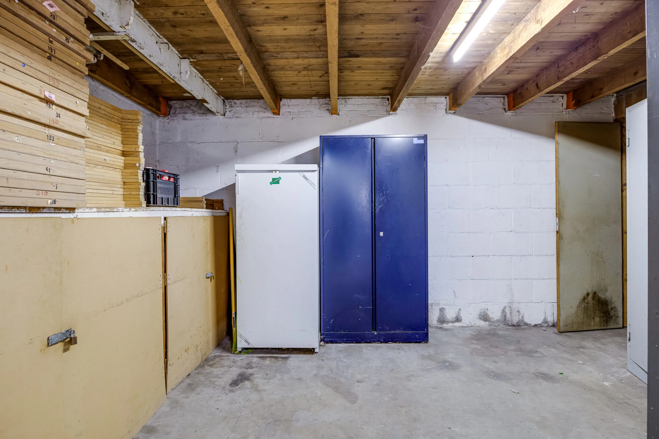 Opbergruimte in een kelder met houten plafond, metalen kasten en gestapelde houten planken aan de Balderikstraat.