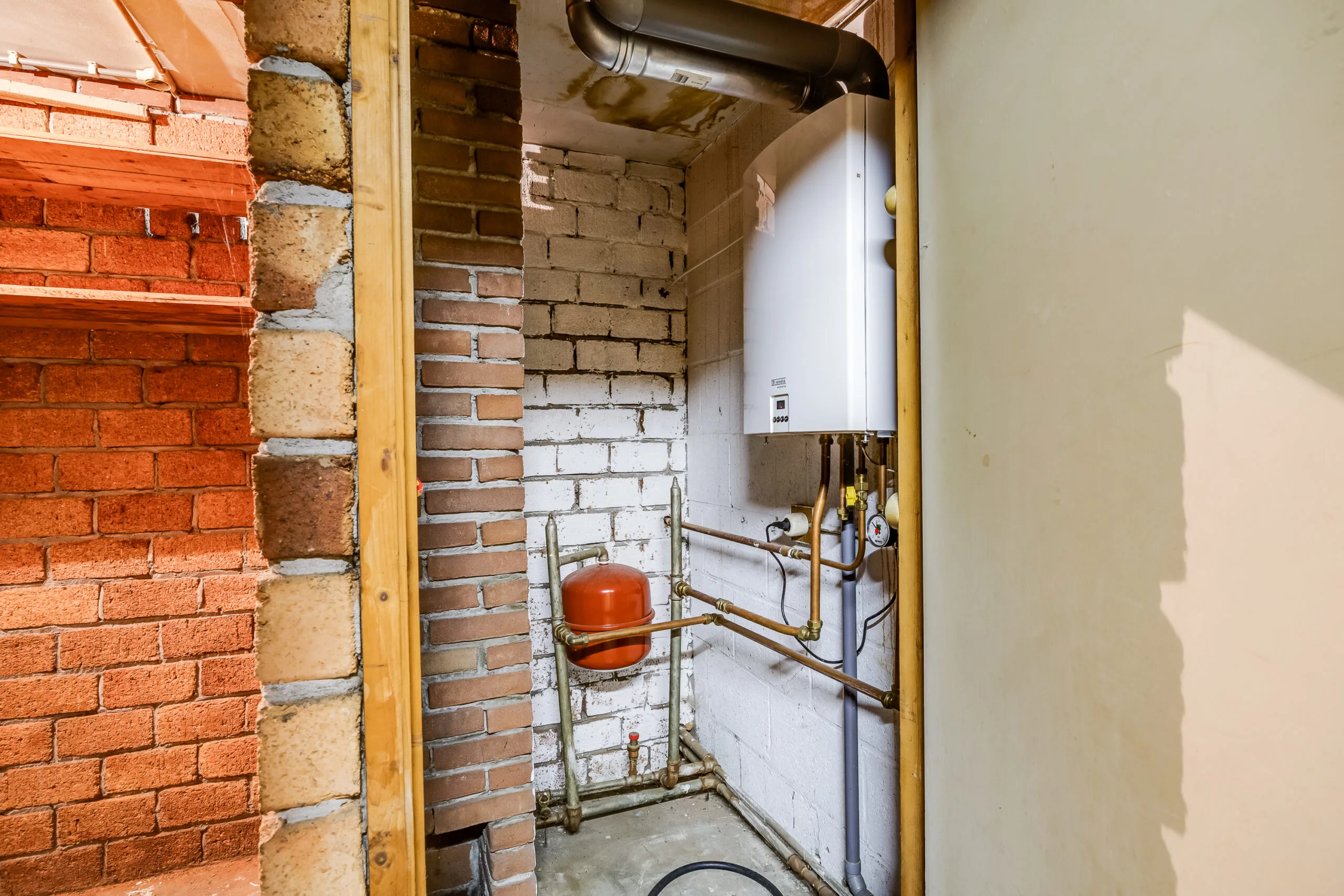 CV-installatie met expansievat en leidingen in een met bakstenen afgewerkte hoek van een ruimte aan de Balderikstraat.