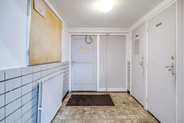 Entreehal met drie witte deuren, een radiator, een prikbord en een vloer met verouderde tegels in een gebouw aan de Balderikstraat.