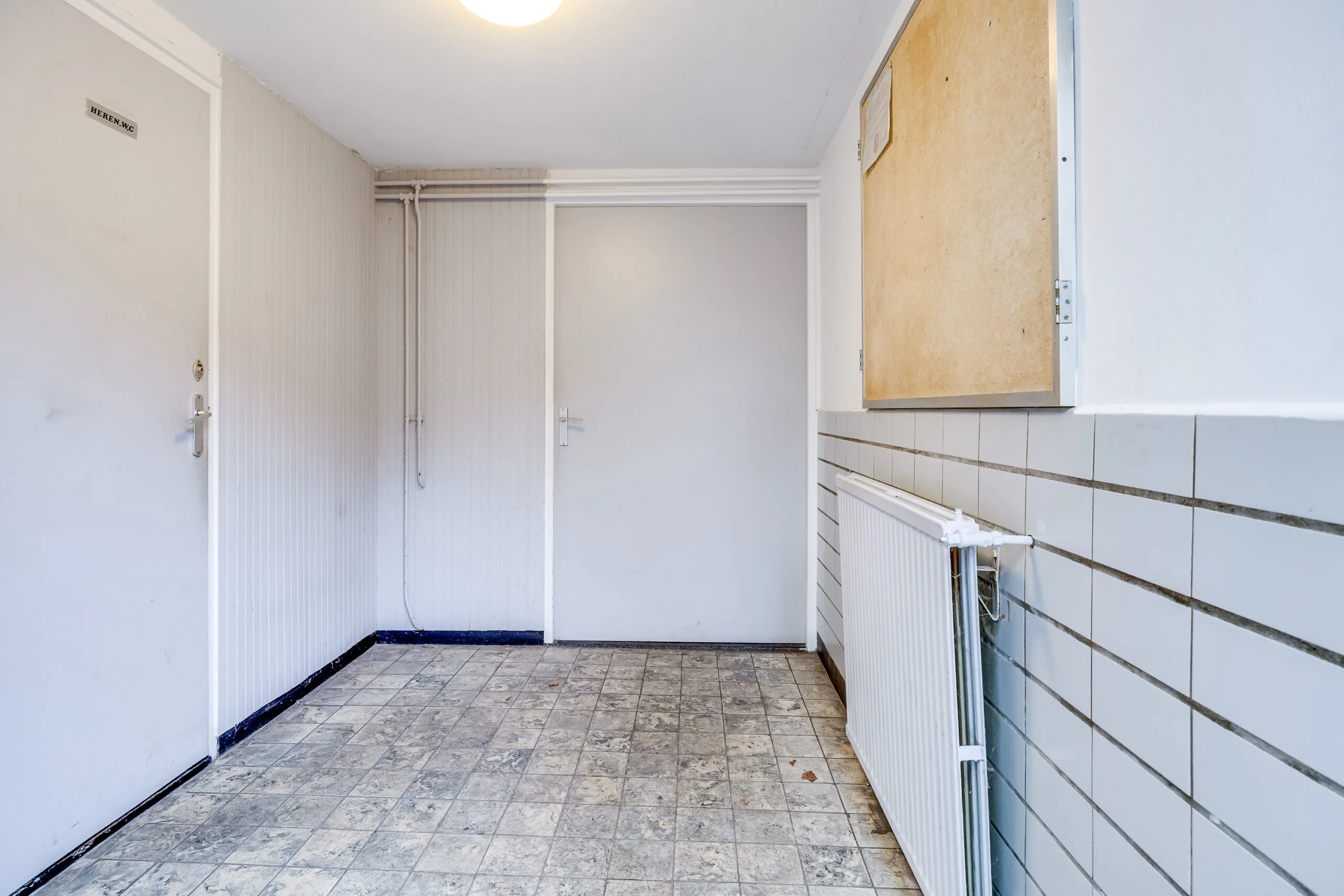 Hal met betegelde vloer in een ouder gebouw aan de Balderikstraat, met deuren en een radiator aan de muur.