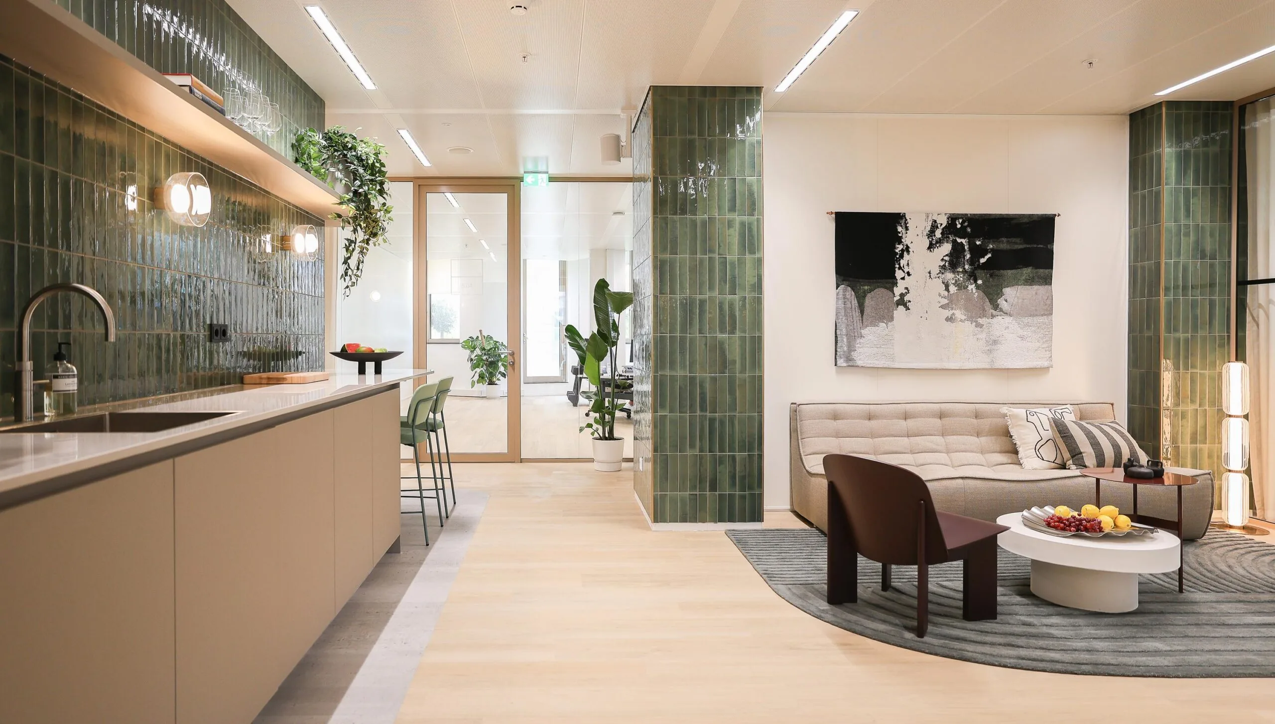Moderne woonkamer en keuken met groene tegels, neutrale meubels en planten.