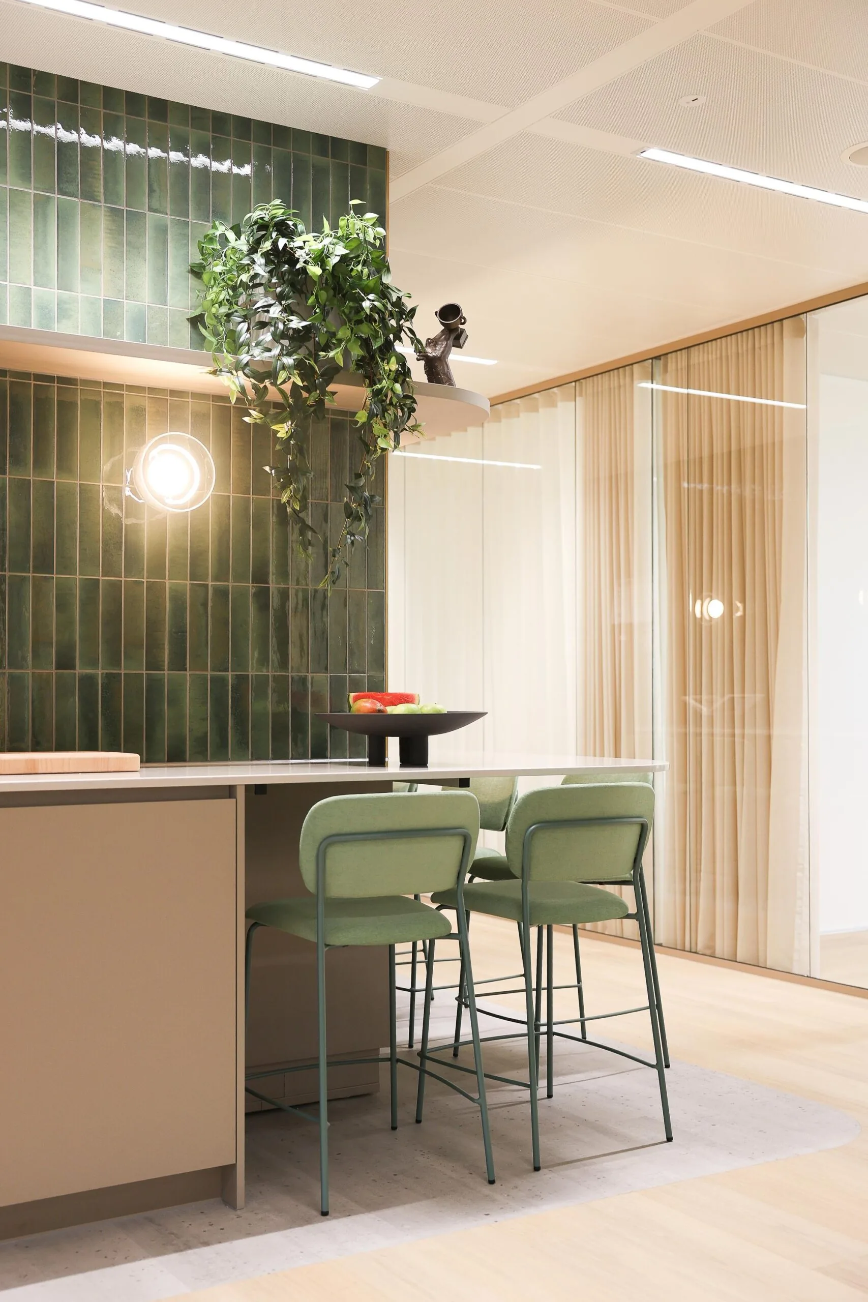 Een moderne keuken met groene tegels, een hangende plant, en een zitgedeelte met groene stoelen.
