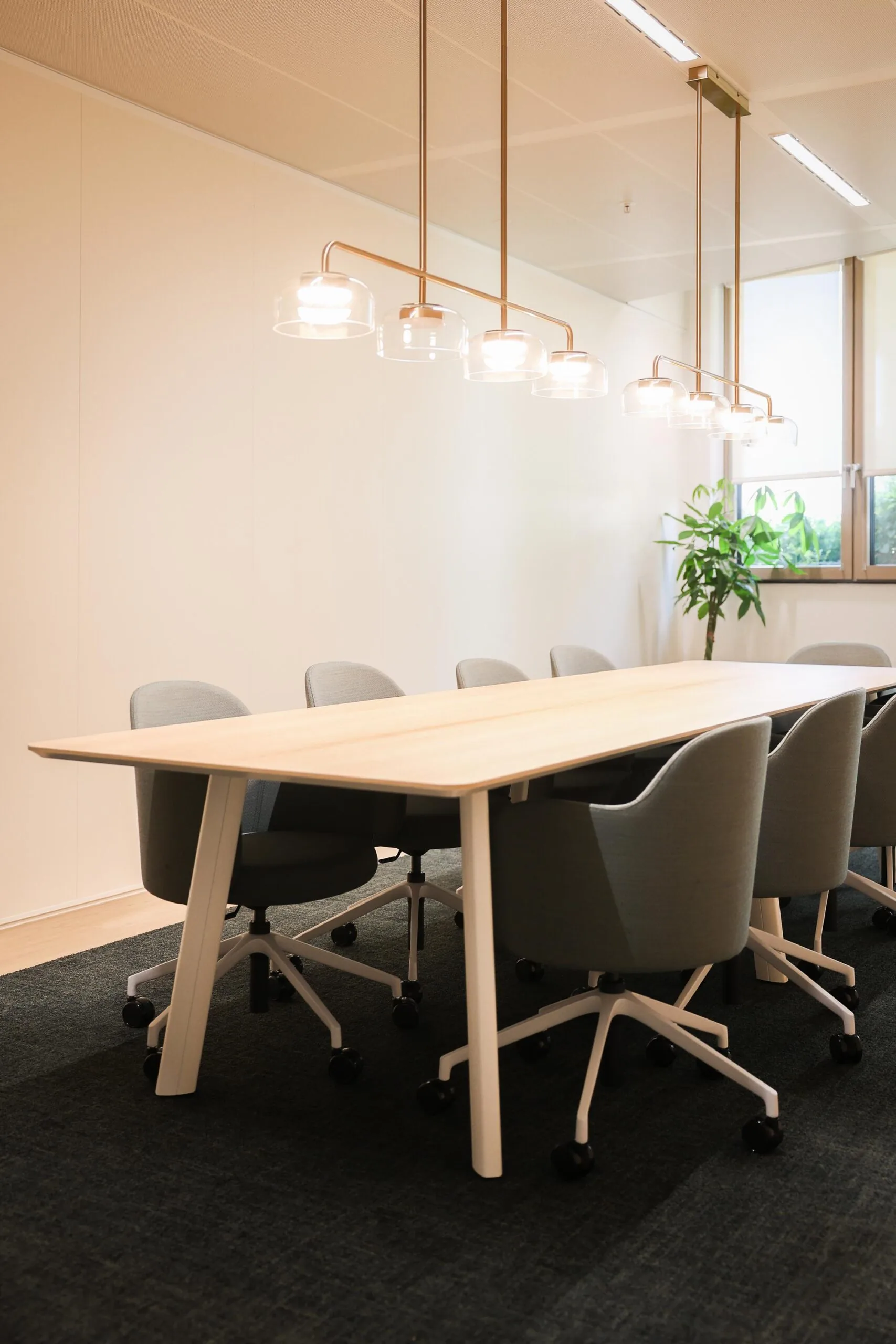 Een vergaderruimte met een houten tafel, grijze stoelen en moderne hanglampen.