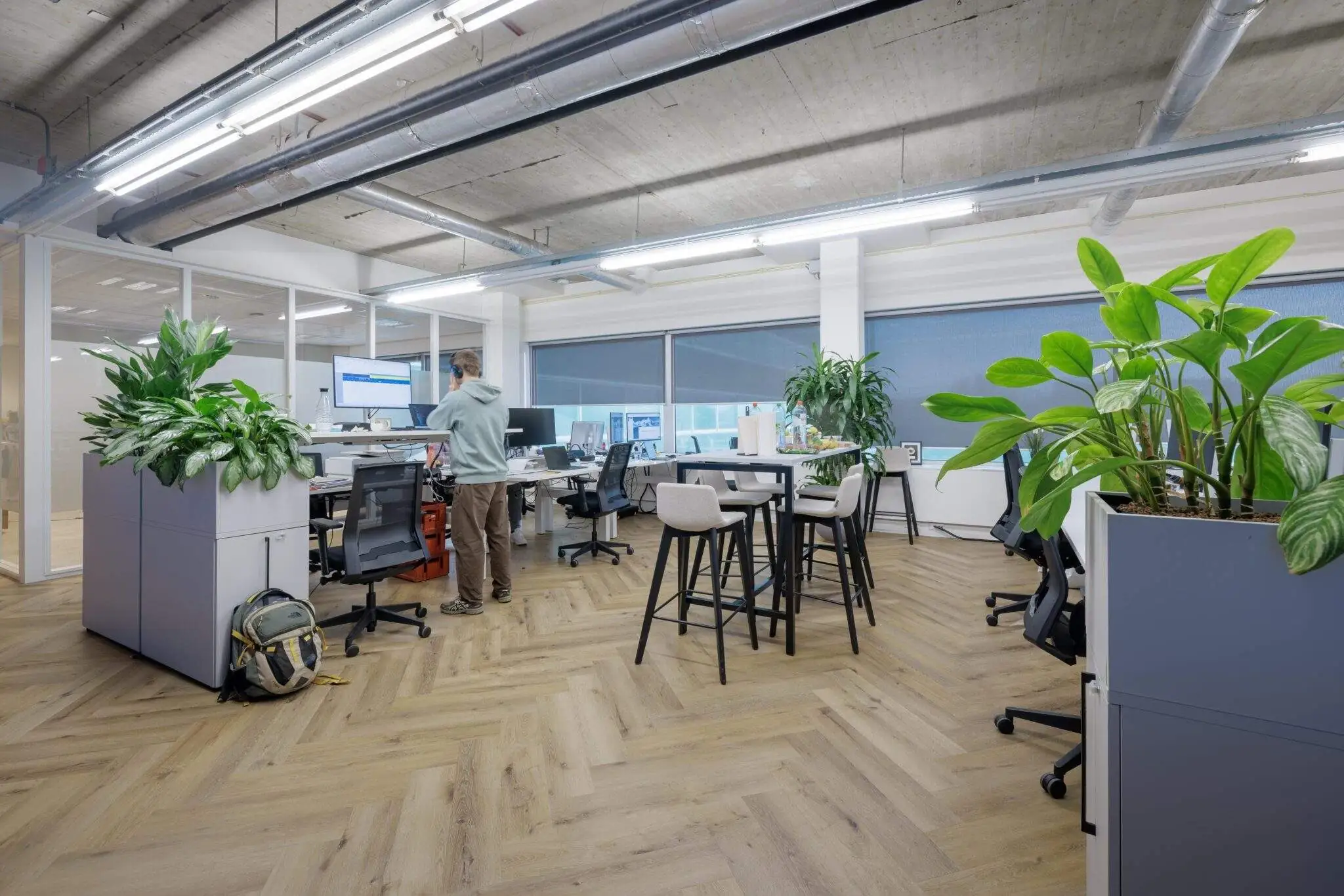 Een modern kantoorinterieur met veel planten, houten vloer en een persoon aan het werk bij een bureau.